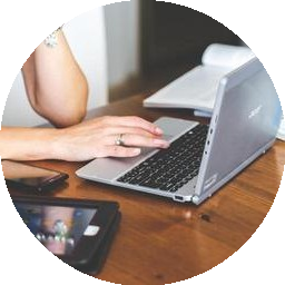 Person using a laptop on a wooden table, with a tablet nearby.