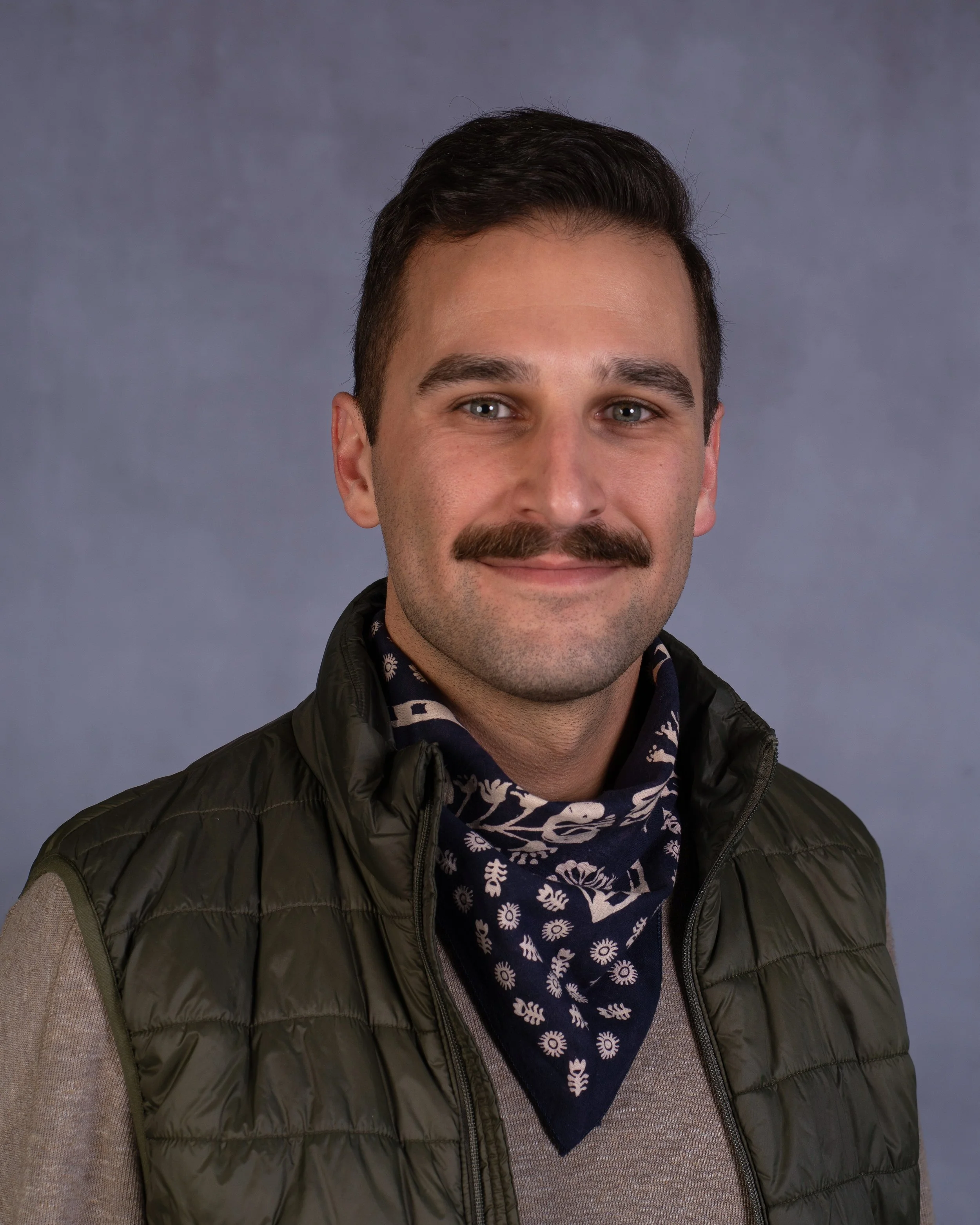 Portrait of Michael Mirza wearing a vest and patterned bandana