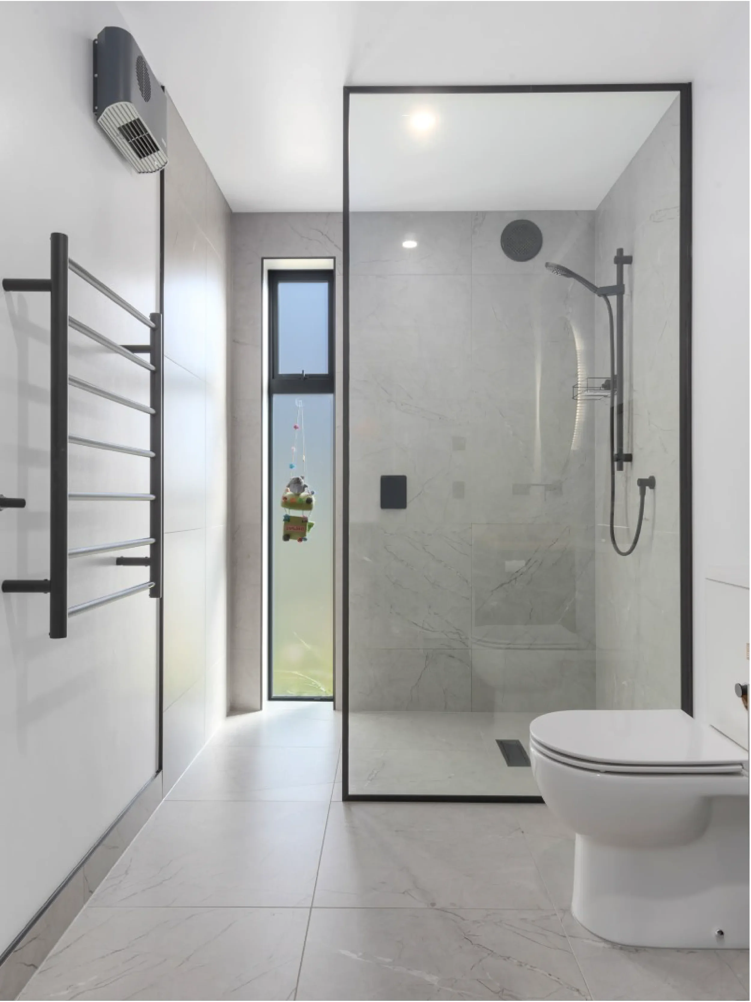 Modern bathroom with a glass shower enclosure and wall-mounted toilet, marble tiles, a towel radiator, a window, and minimalist decor.