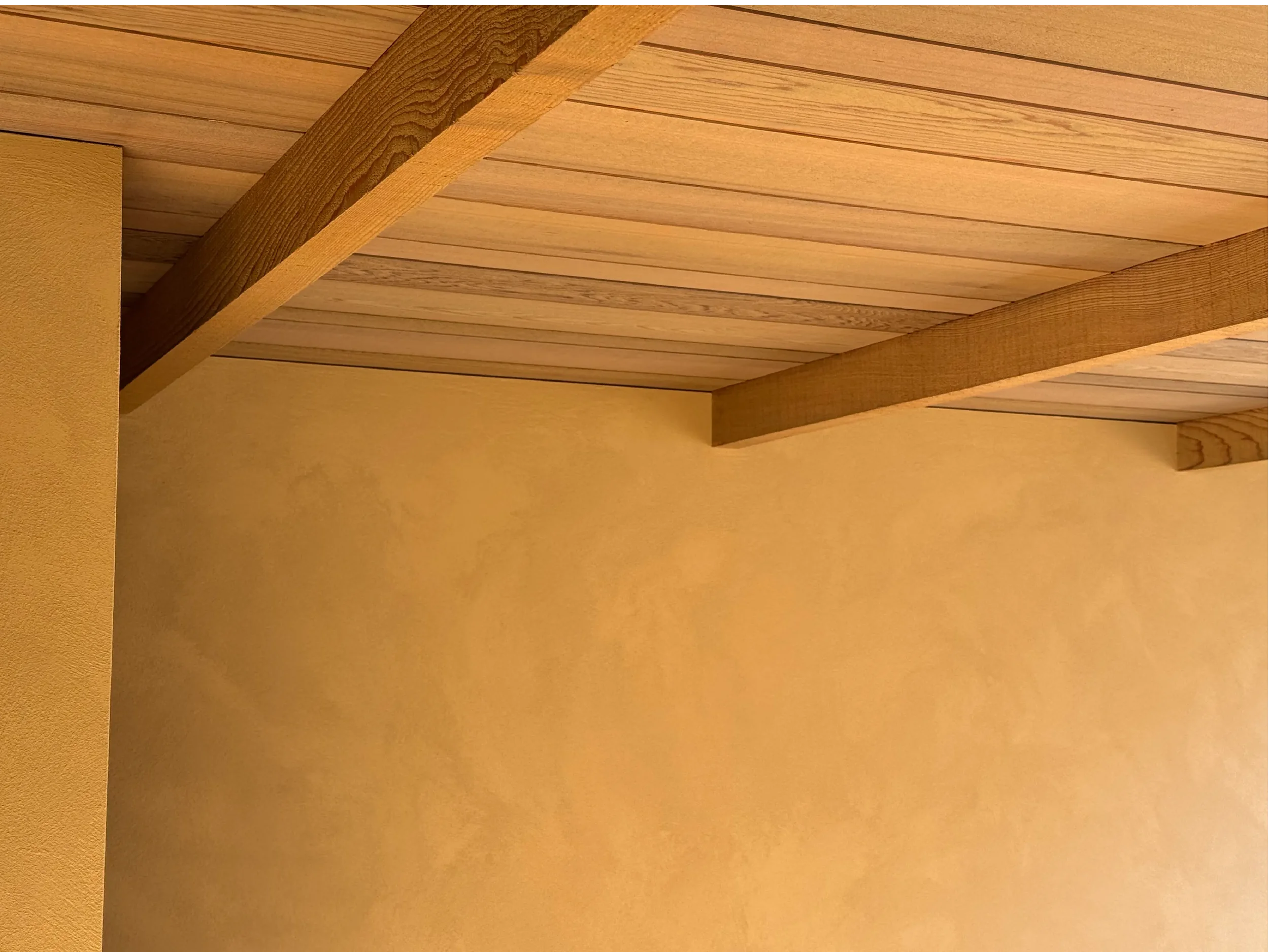 A ceiling with wooden planks and beams, painted in light beige or tan color.