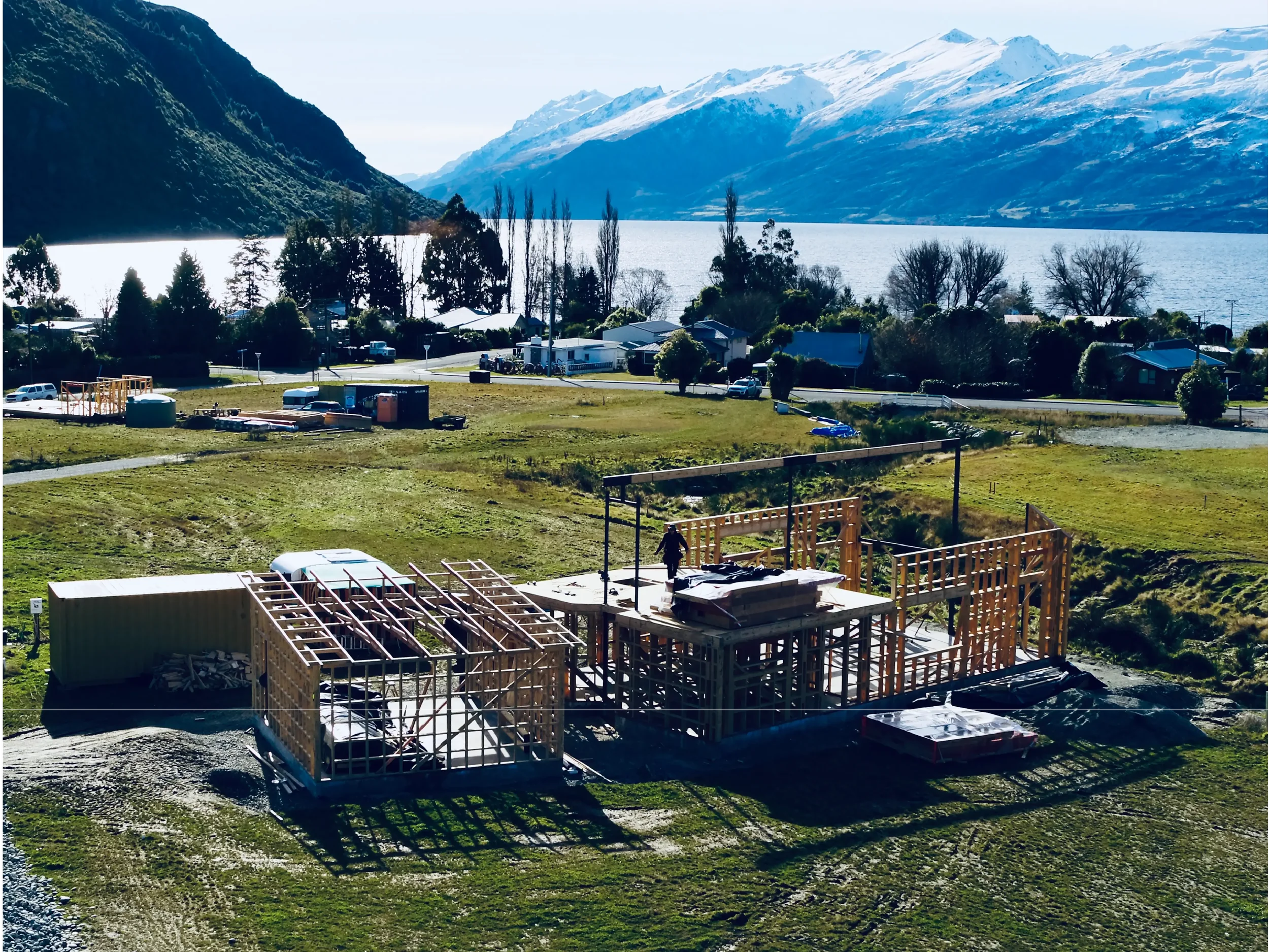 Construction site in a rural area with houses, trees, and mountains in the background, with some building framework and equipment.