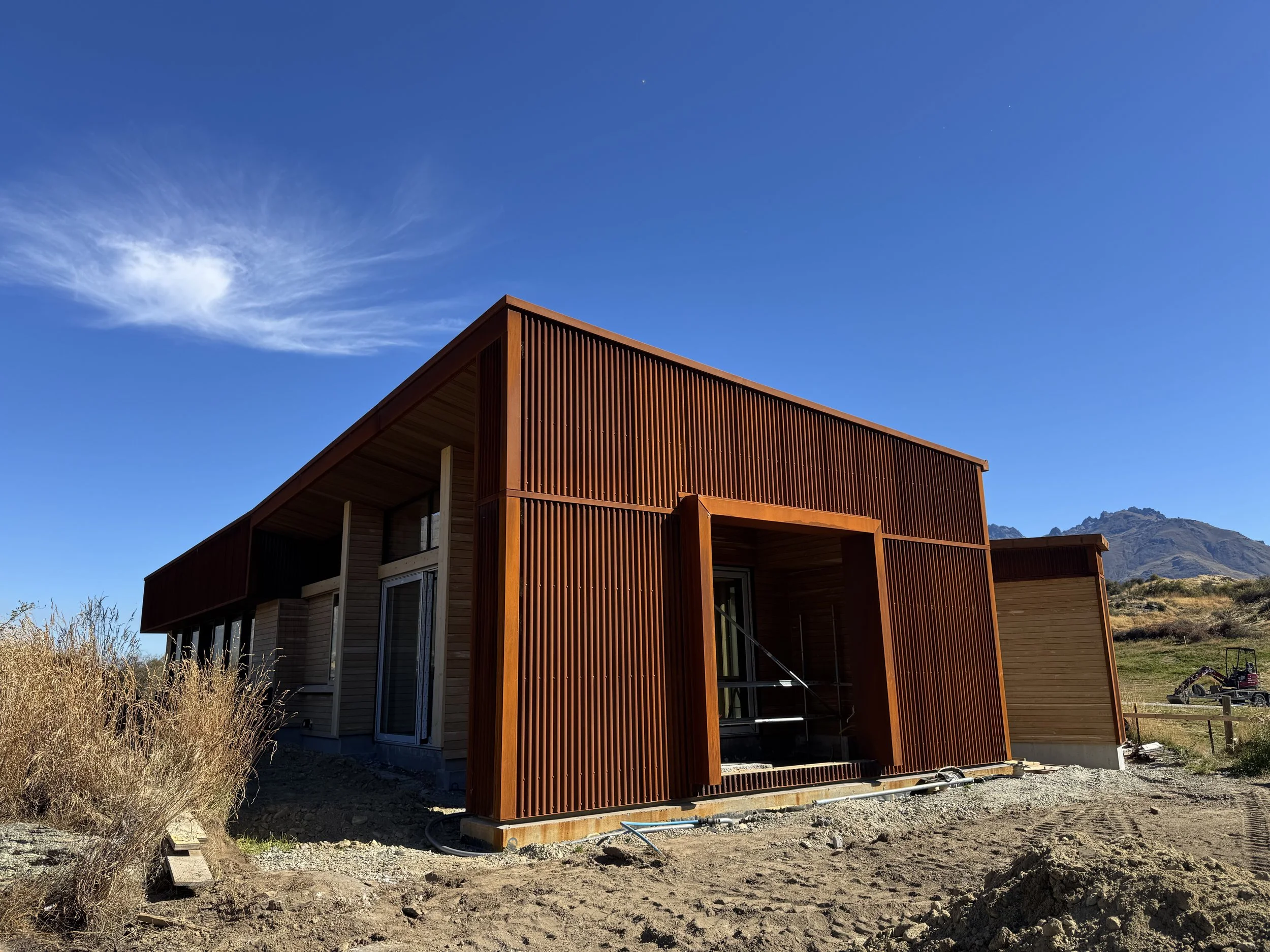 A modern wooden house under construction with a bright blue sky and mountains in the background.