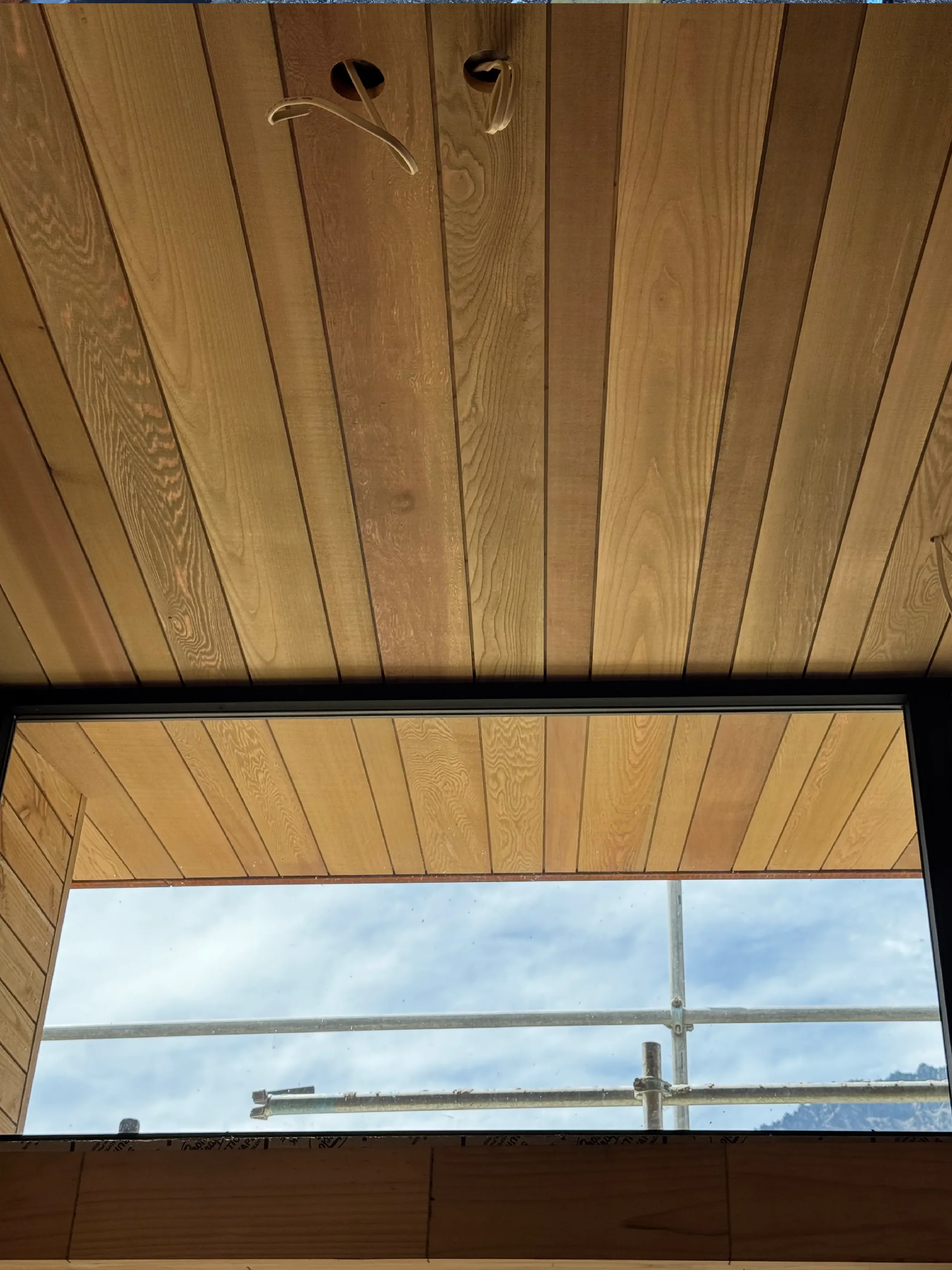 Construction scaffolding with wooden panels and a window showing a cloudy sky.