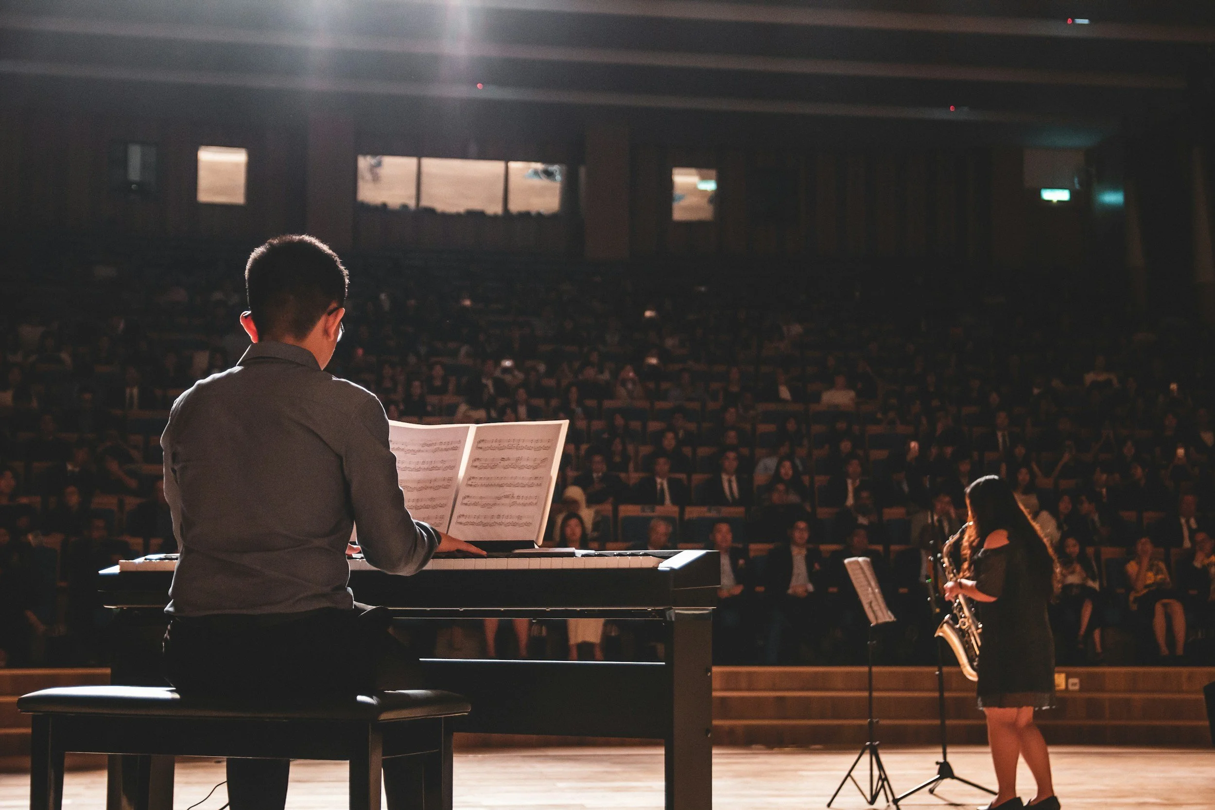 A man playing the piano on stage with an orchestra in front of a large audience in a concert hall