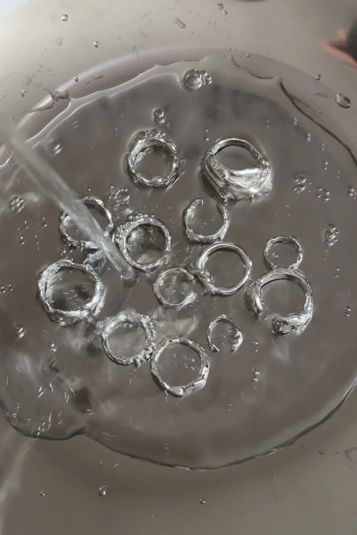 Close-up of a sink filled with water, holding several silver rings submerged in water.