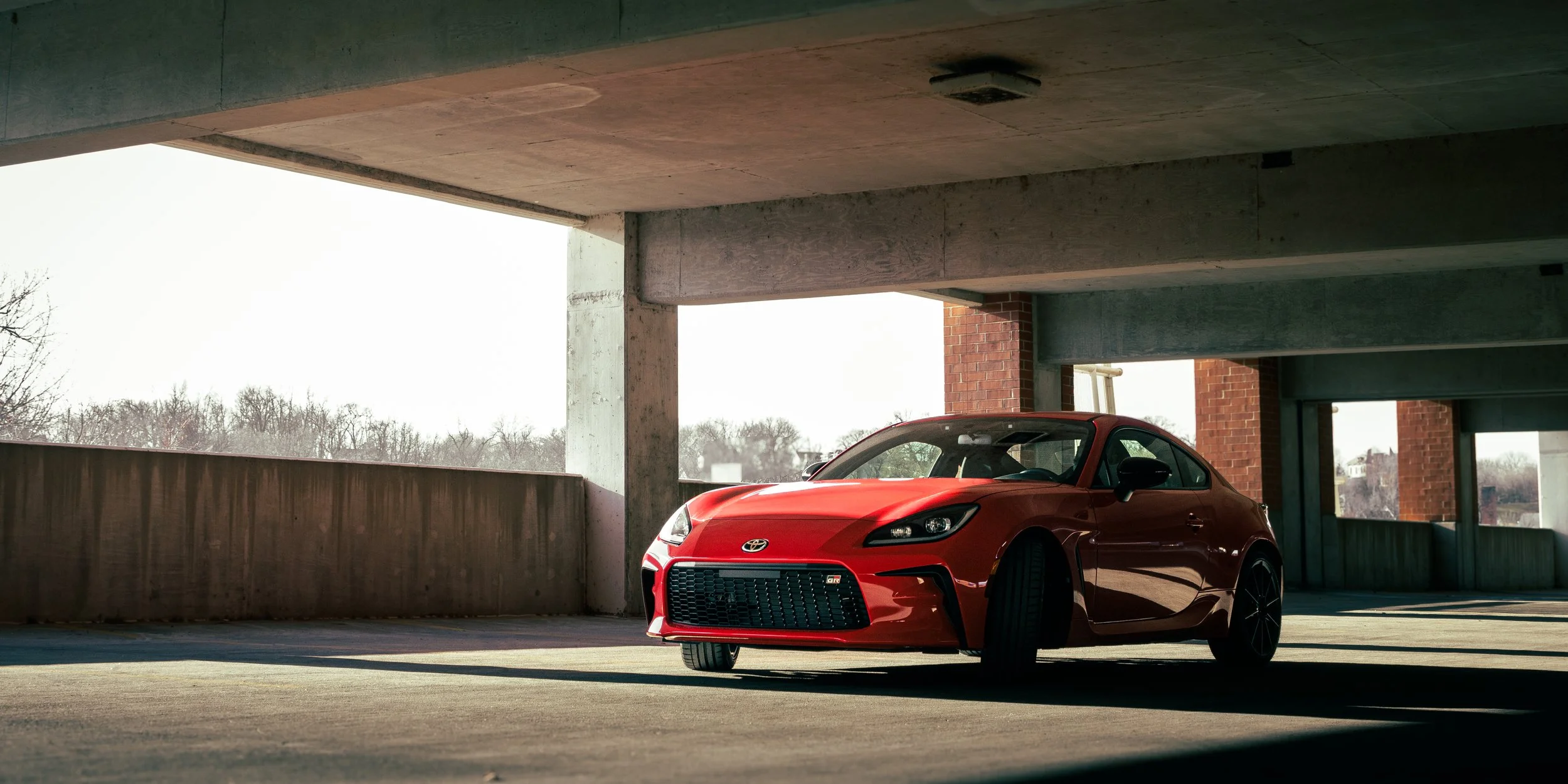 A red Toyota GR86 parked in an indoor parking garage.