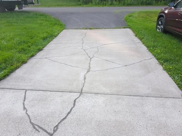Cracked concrete driveway with grass on either side and a parked car on the right.