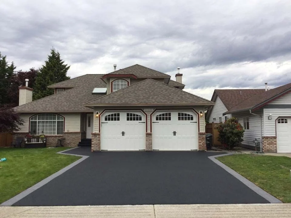 Two-story house with a double garage, manicured lawn, and a paved driveway under cloudy sky.