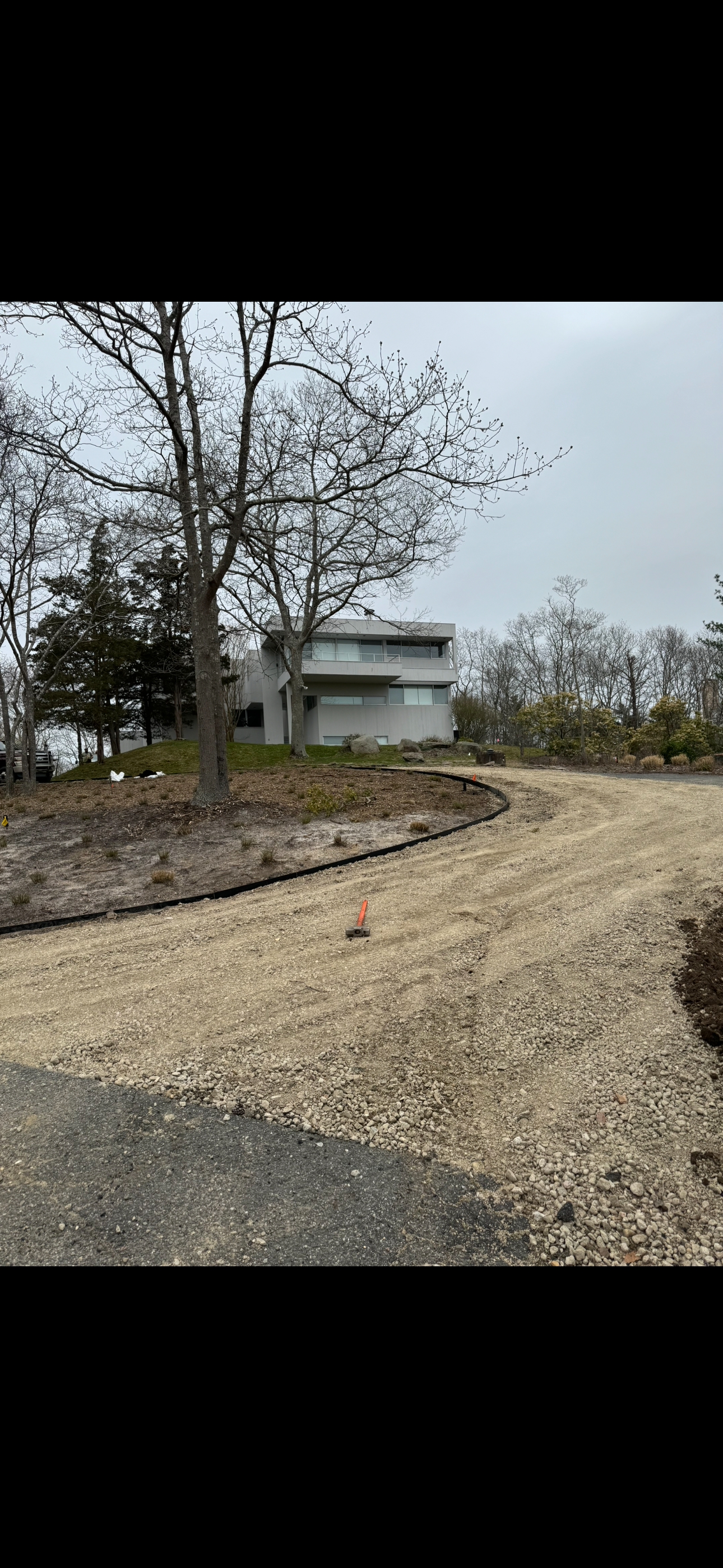 A modern house under construction with a dirt road and bare trees, and construction markers in the foreground.