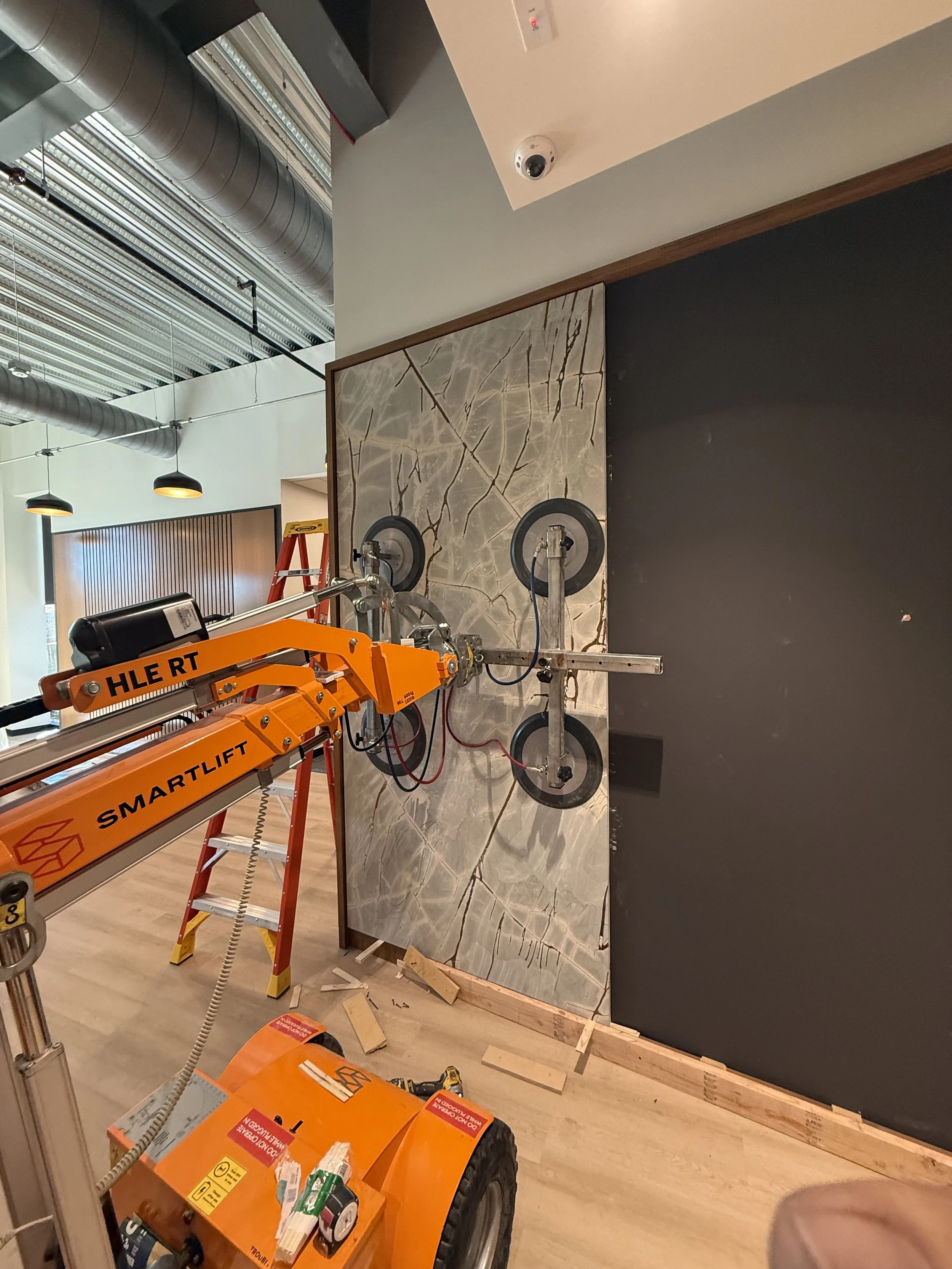 Construction scene showing a tile adhesive removal machine on a tile wall, with tools and a ladder nearby, in an indoor space.