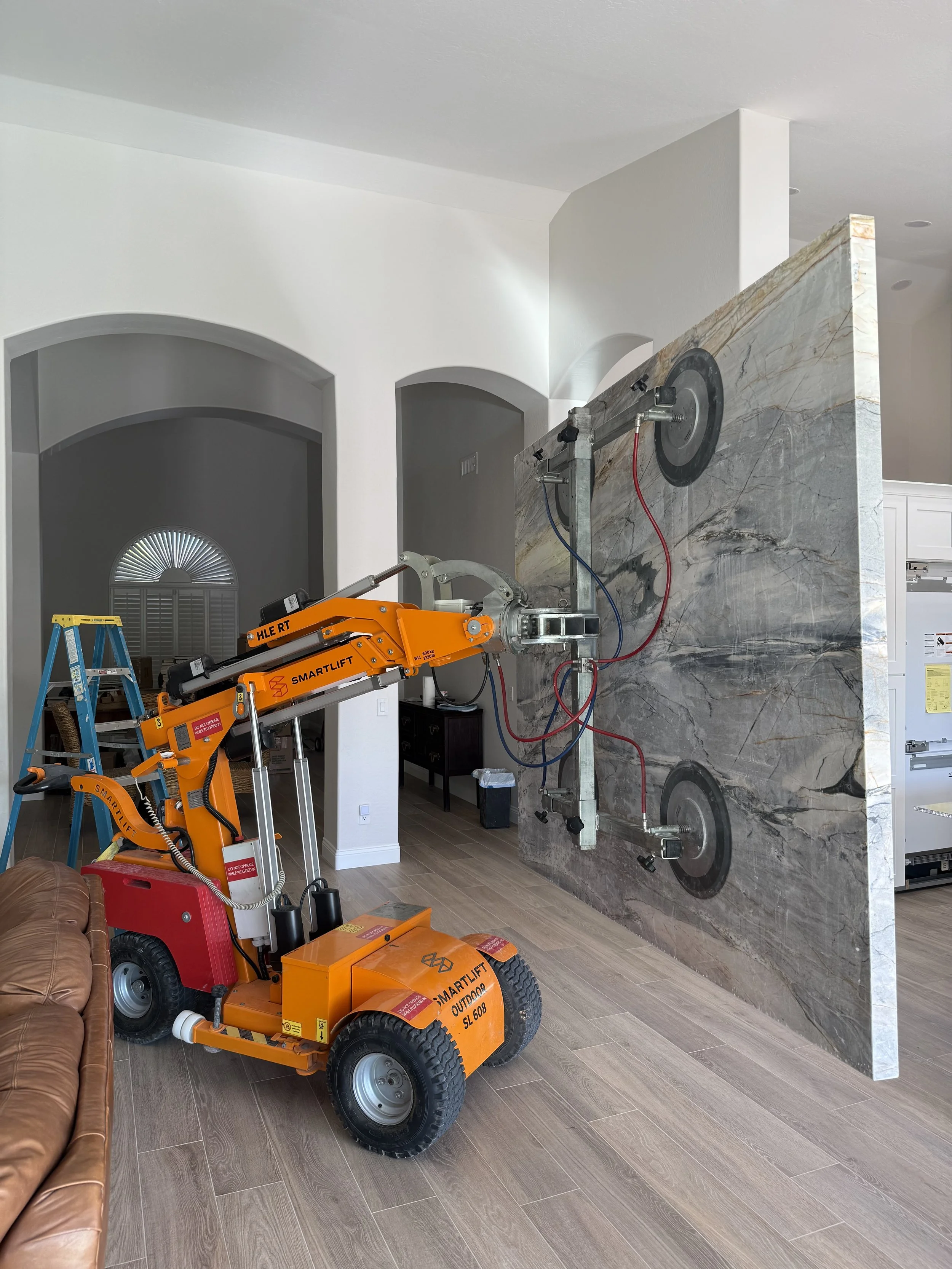 Construction equipment in a living room pushing a large marble or granite slab against a wall.