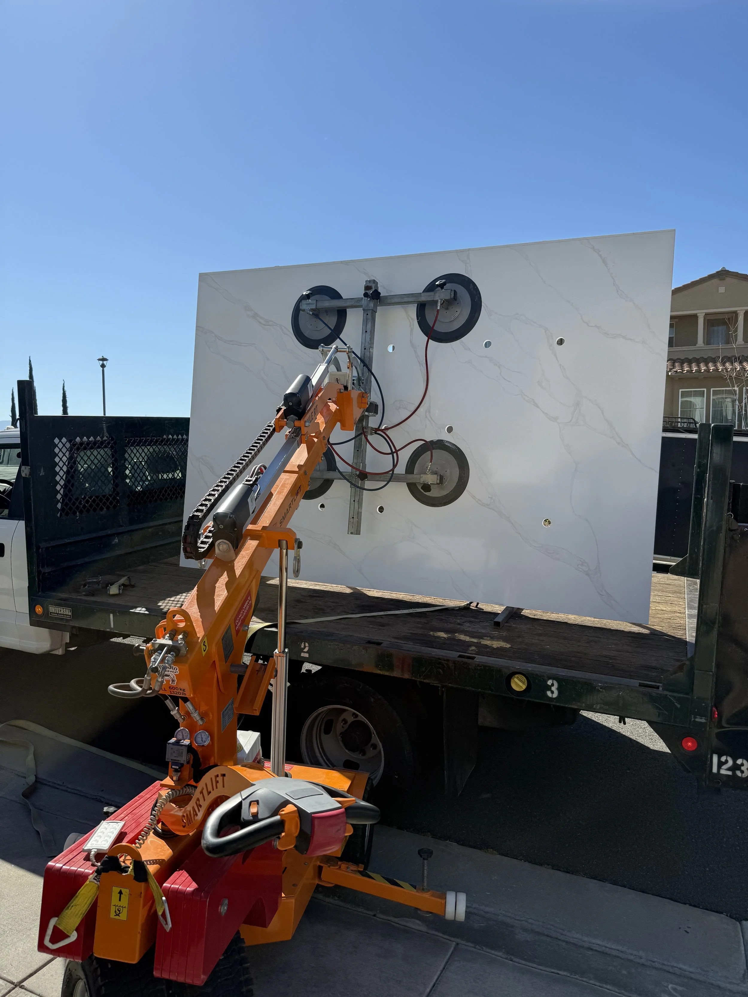 A large marble or quartz panel with a marble pattern is being moved or installed using a lift device on a flatbed truck.