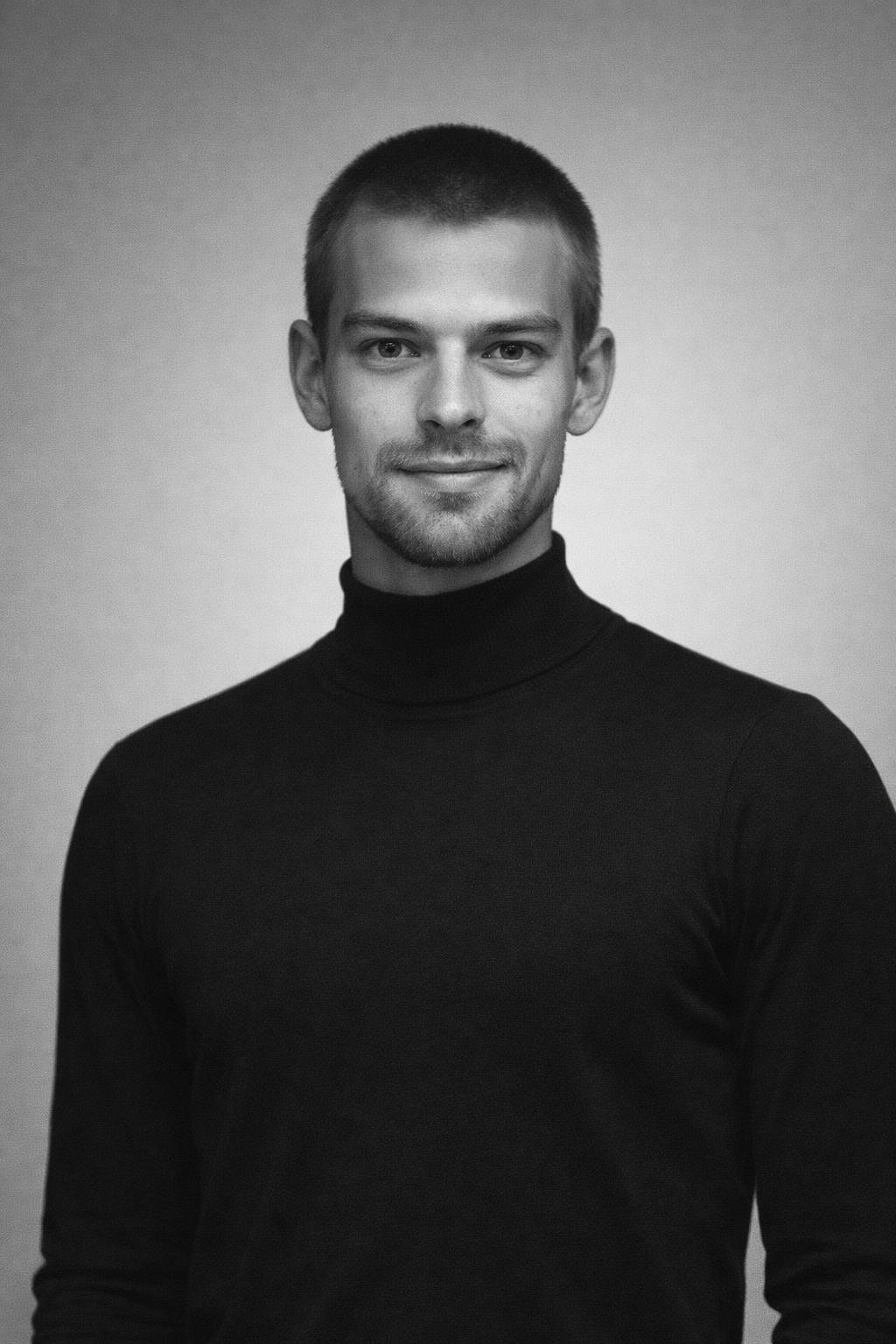Black and white portrait of a young man with short hair, wearing a black turtleneck, looking at the camera with a slight smile.