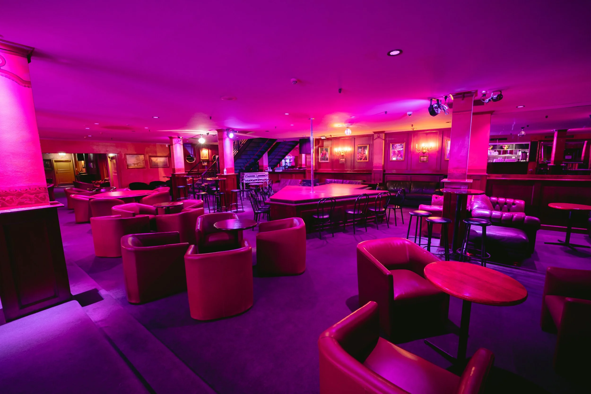Lounge seating area with tables under pink lighting at The Men's Gallery Melbourne strip club