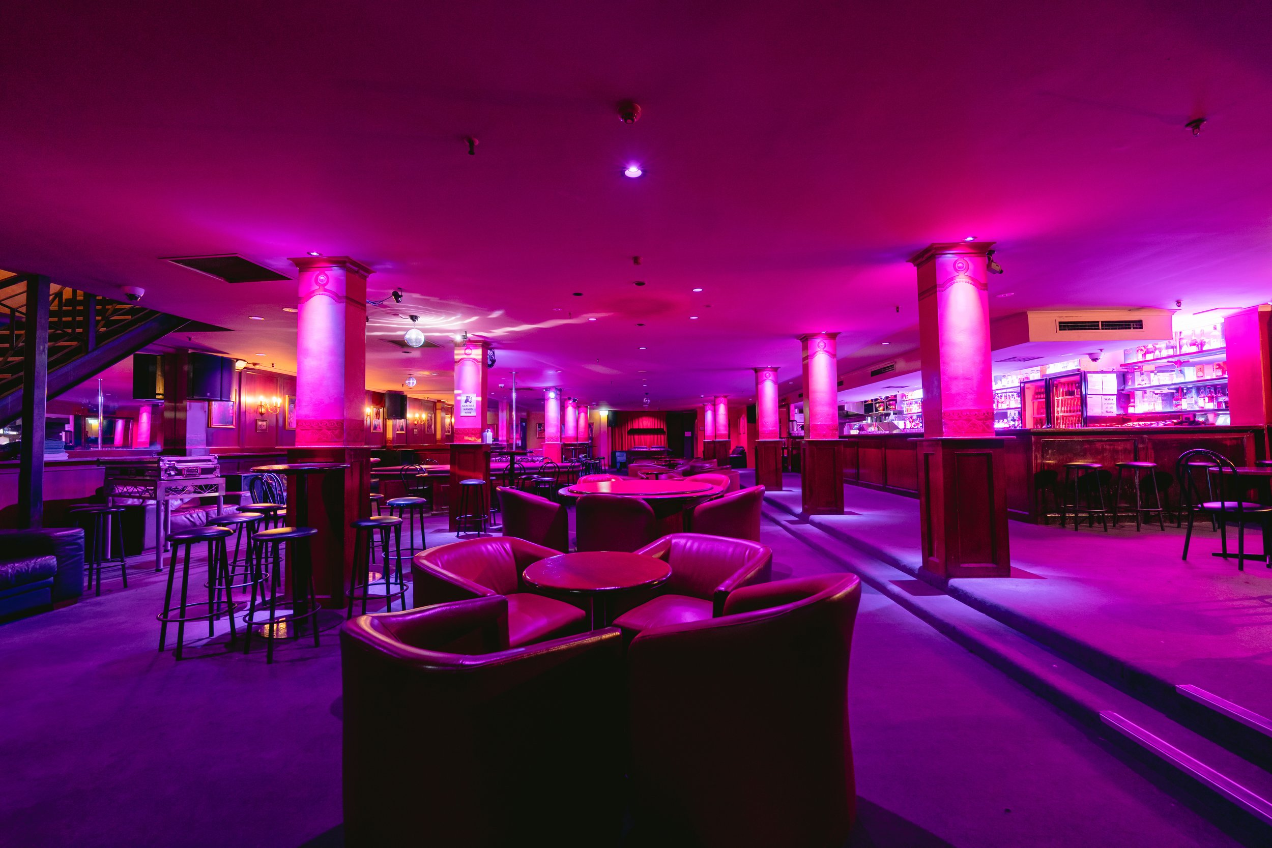 Booth seating near the bar under purple lighting at The Men's Gallery Melbourne strip club