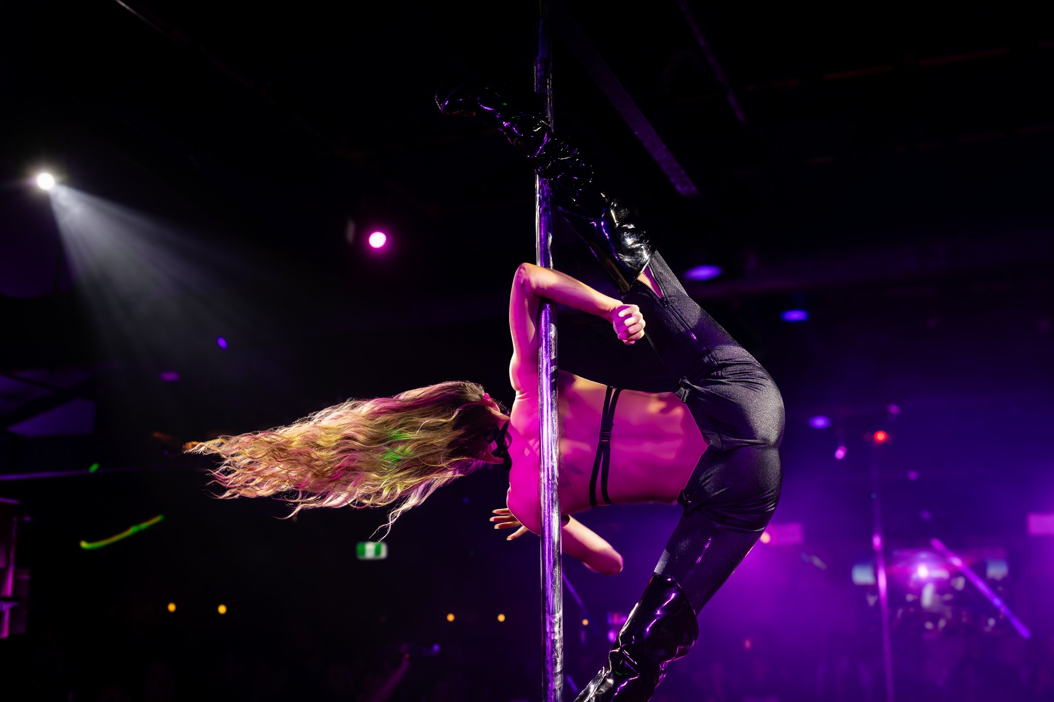 Pole performer with flowing hair under pink stage lighting at The Men's Gallery Melbourne strip club