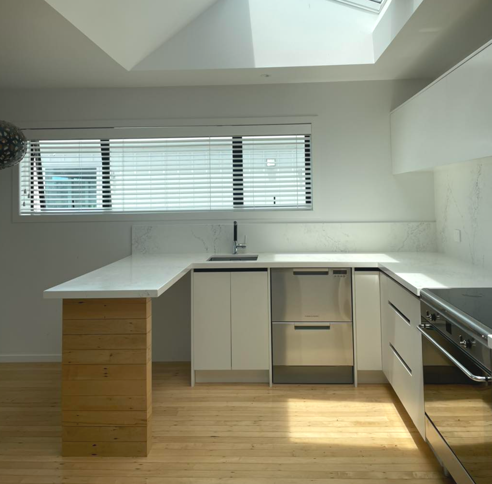 Modern kitchen with white cabinetry, marble countertops, stainless steel appliances, wooden flooring, and a large window with blinds.