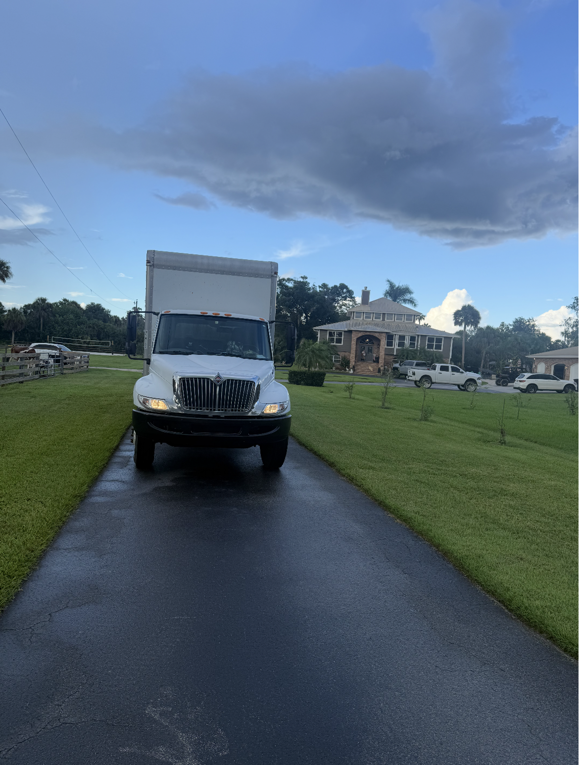 White delivery truck parked on a driveway with a house in the background, under a blue sky with dark clouds.