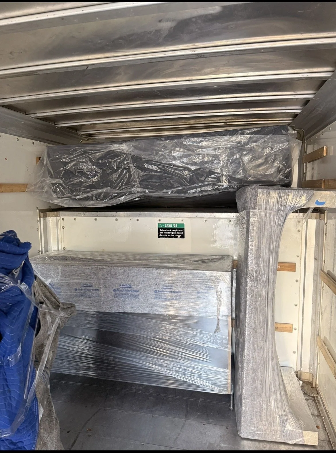Interior view of a truck cargo area with metal shelving and equipment wrapped in plastic for shipment or storage.