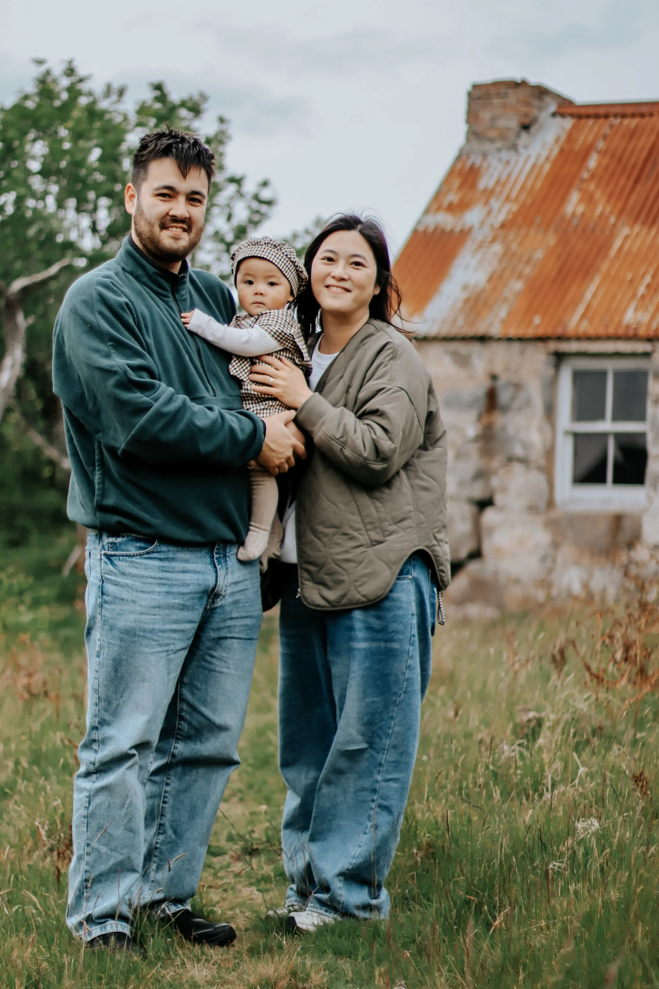 Family photography Scottish Highlands parents holding baby outside rustic cottage bothy in natural light