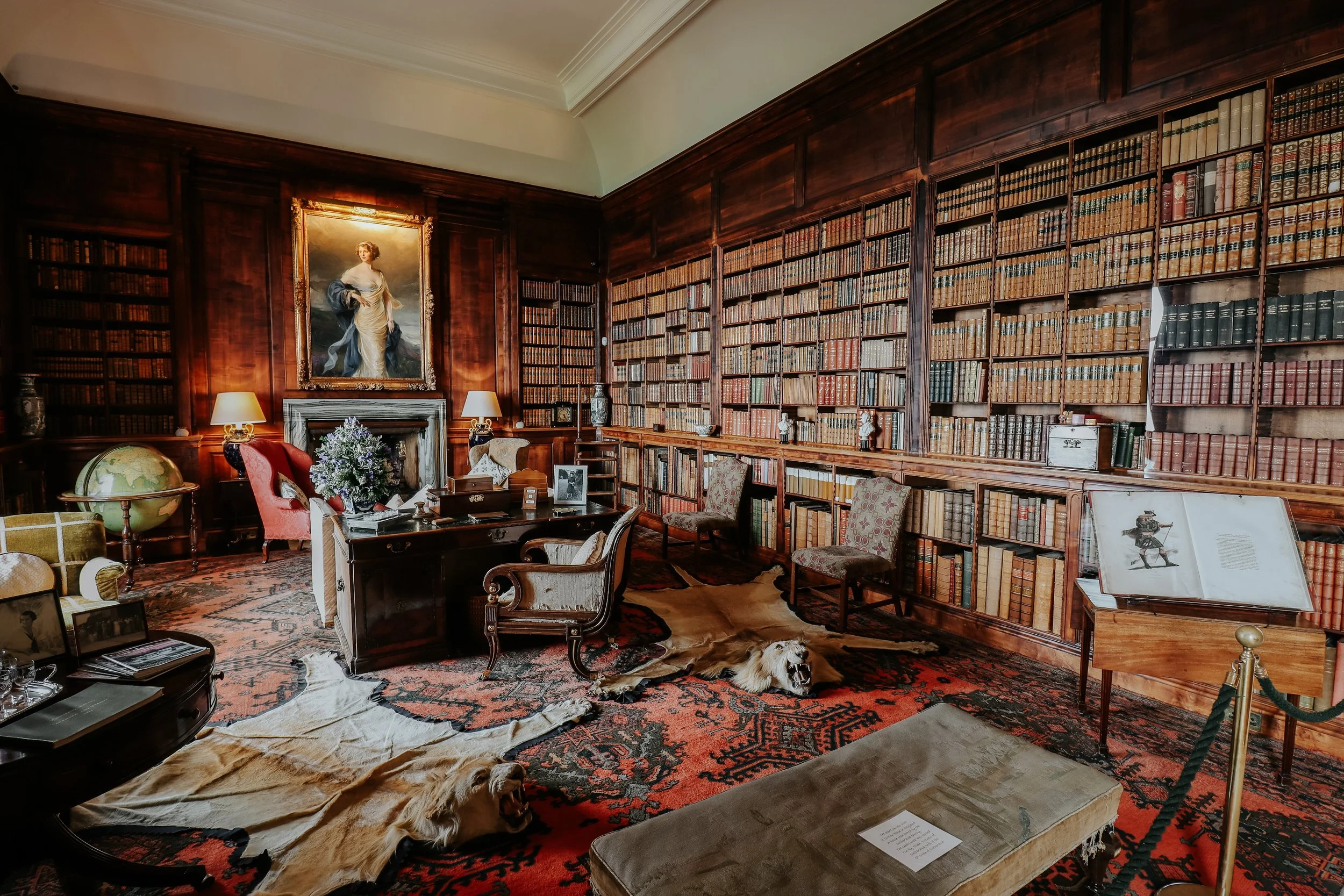 Interior photography of the historic library at Dunrobin Castle, featuring floor-to-ceiling bookshelves, antique furnishings and rich wood panelling.