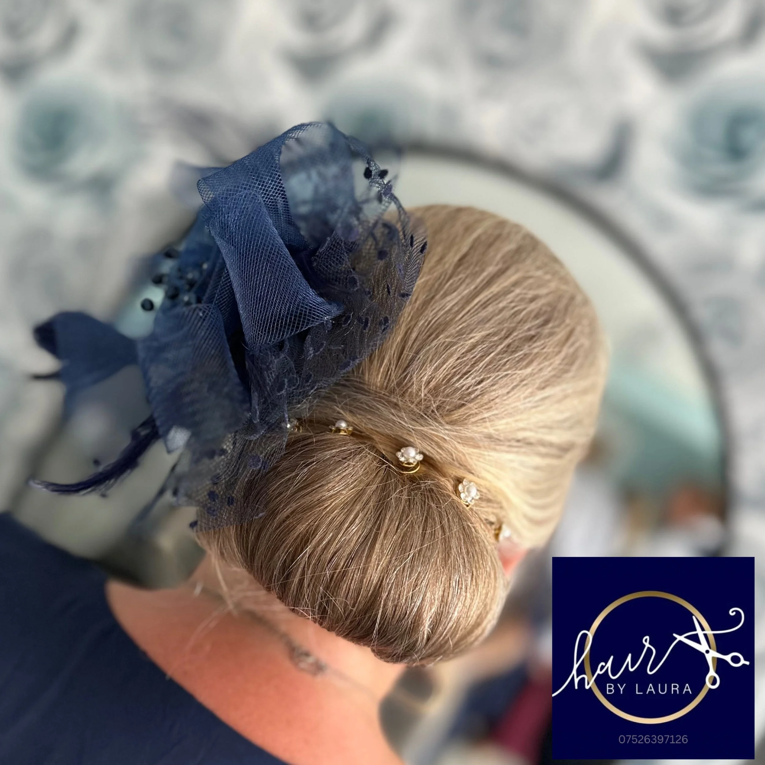 Close-up of a person's hair styled with a pearl hair accessory and lace fabric. The background is blurred with a pattern of white and light blue. Part of a navy blue outfit with white polka dots is visible.