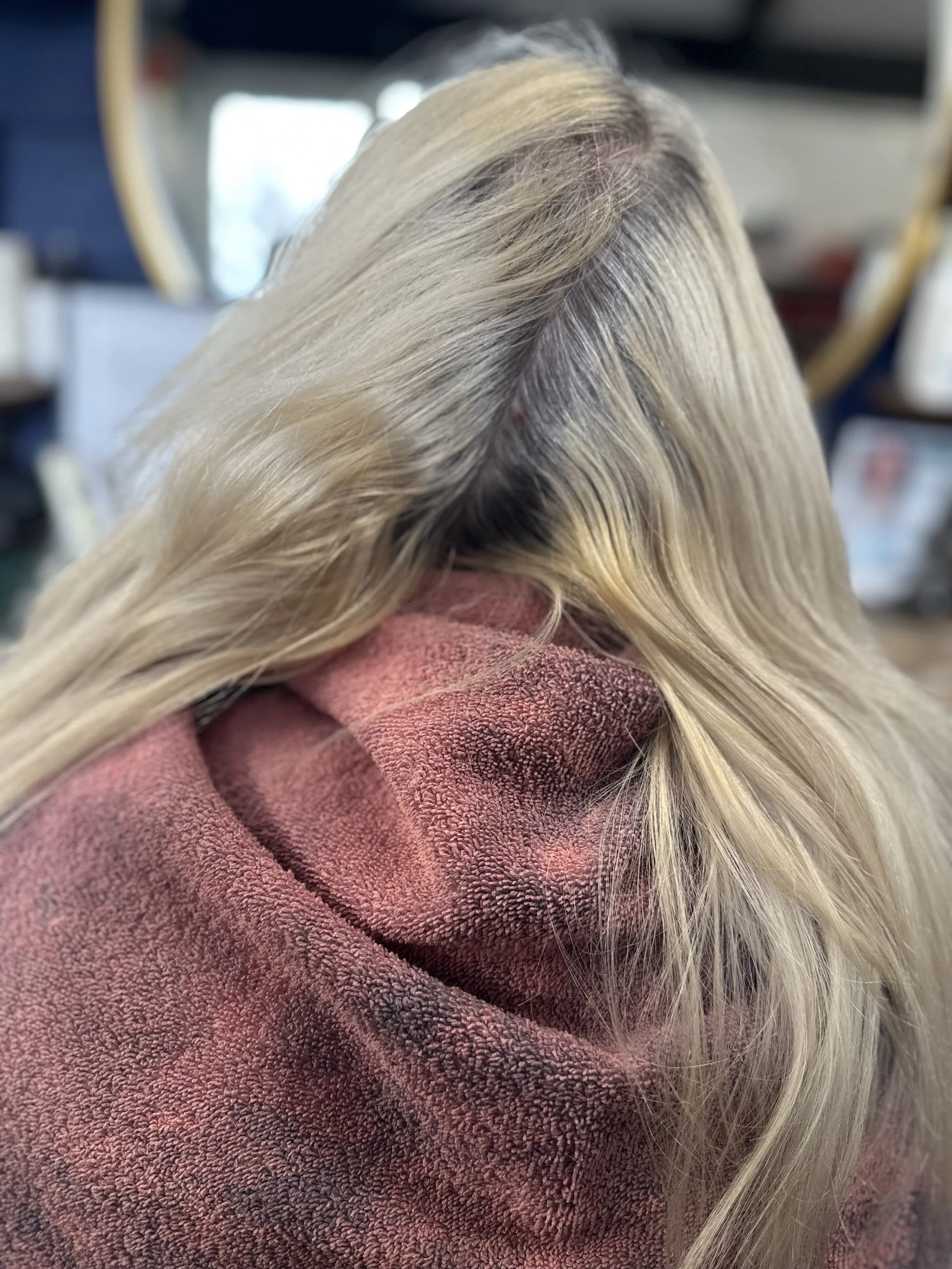 Close-up of a person's blonde hair with highlights, resting on a reddish-brown towel with a textured surface.