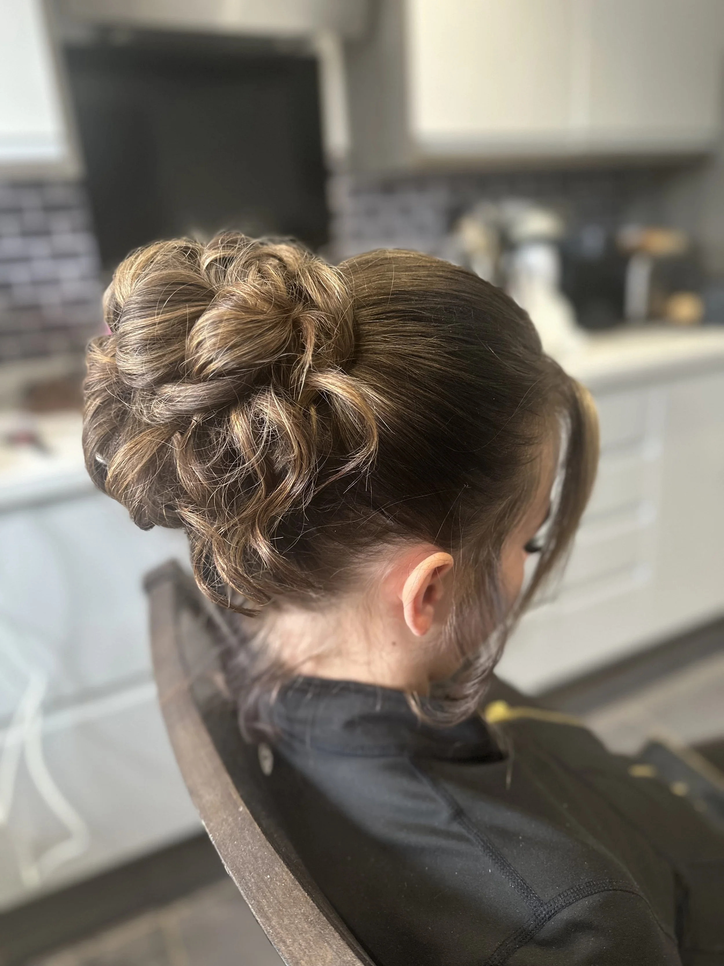 A woman with styled blonde hair, featuring braids and a bun, depicted from the side view, in a kitchen setting.
