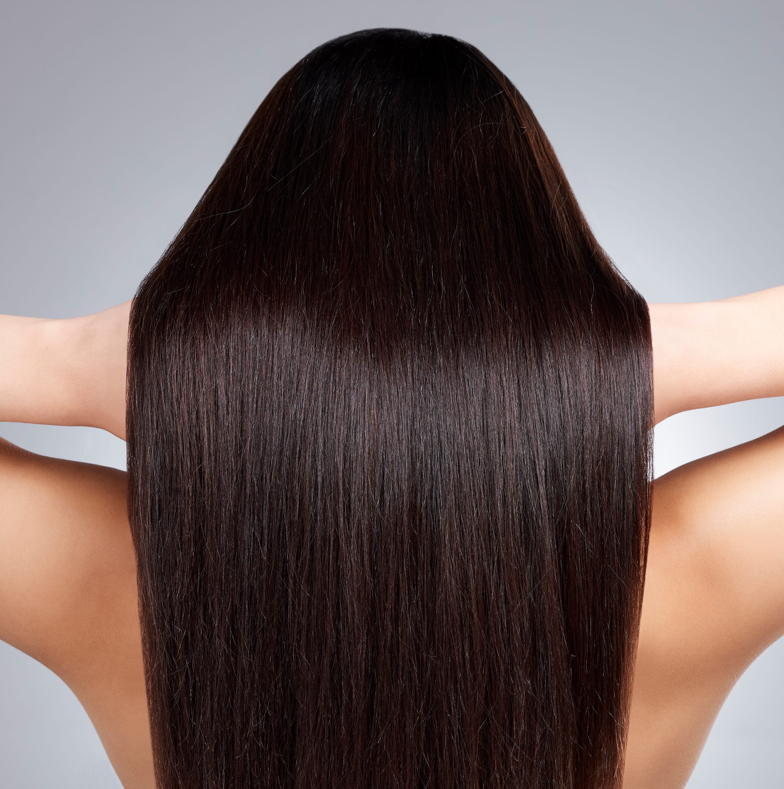 Close-up of a person's long, dark, and shiny hair falling over their shoulders, with a gray background.