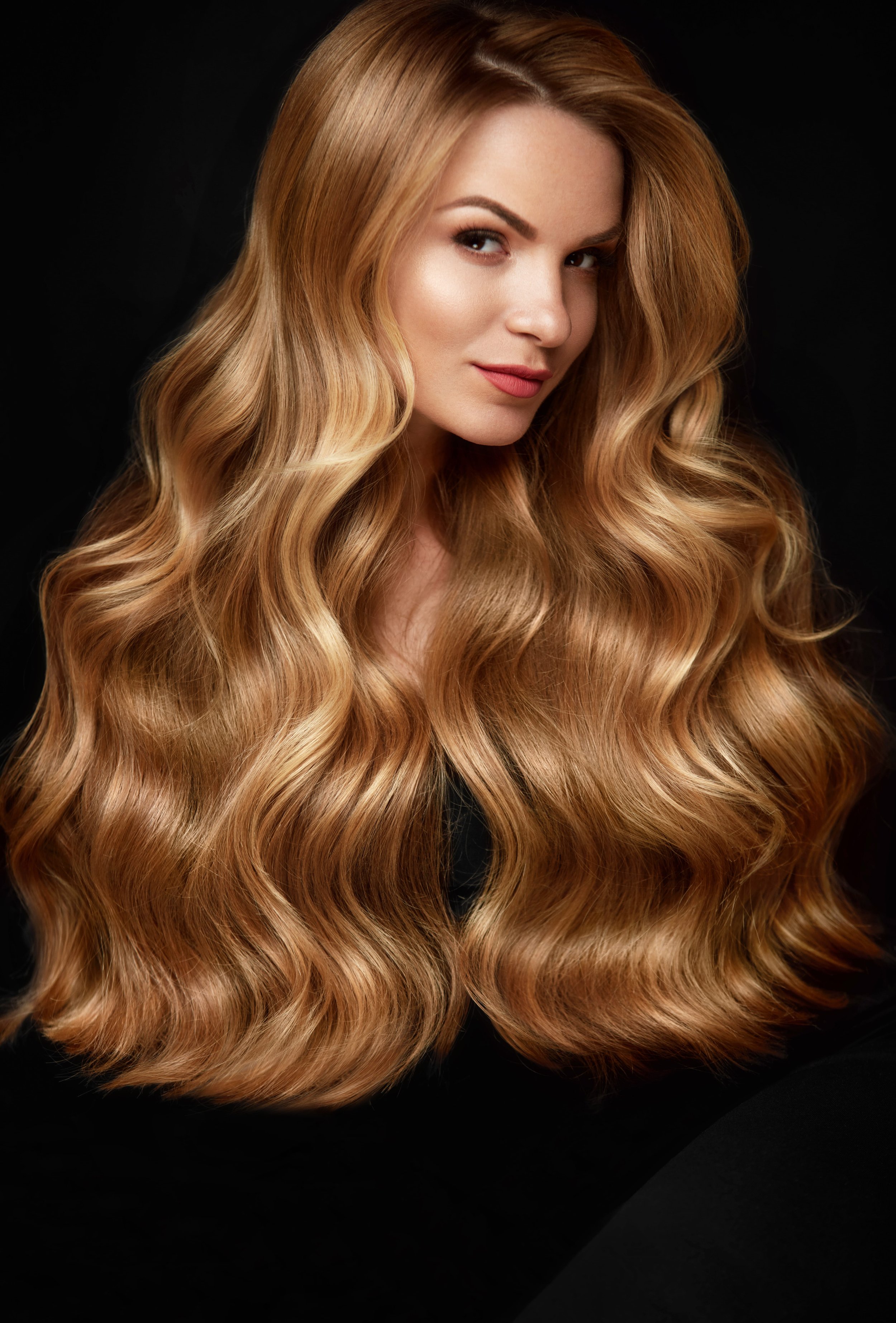 A woman with long, wavy, strawberry blonde hair poses against a black background.