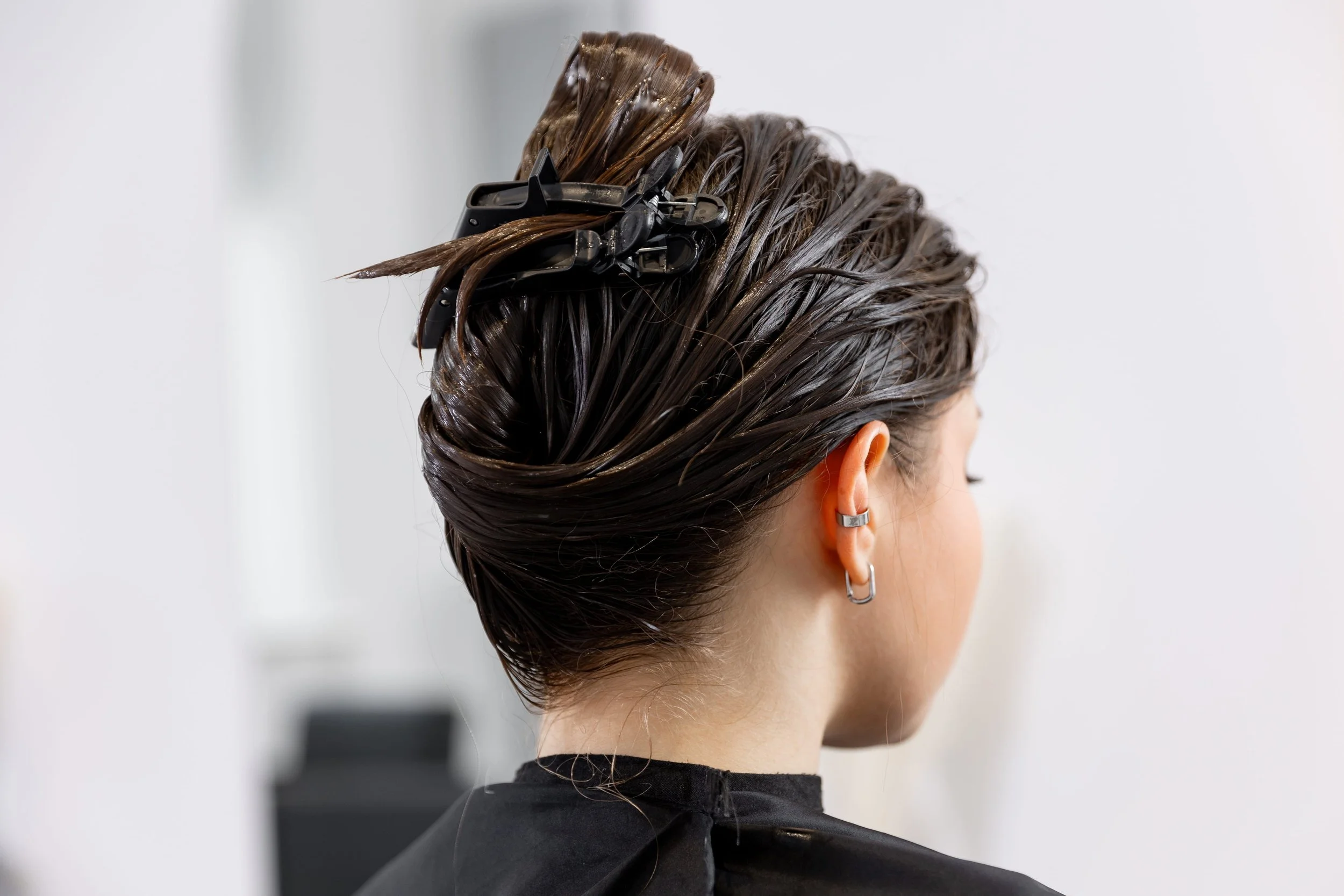 A woman has her hair sectioned with black hair clips while getting her hair dyed or styled at a salon.