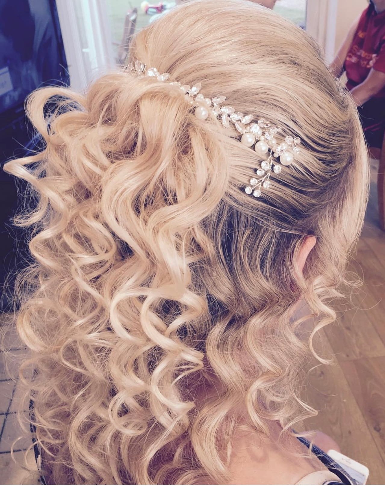 Close-up of a woman with long, blonde, curly hair styled with a pearl and crystal headband.