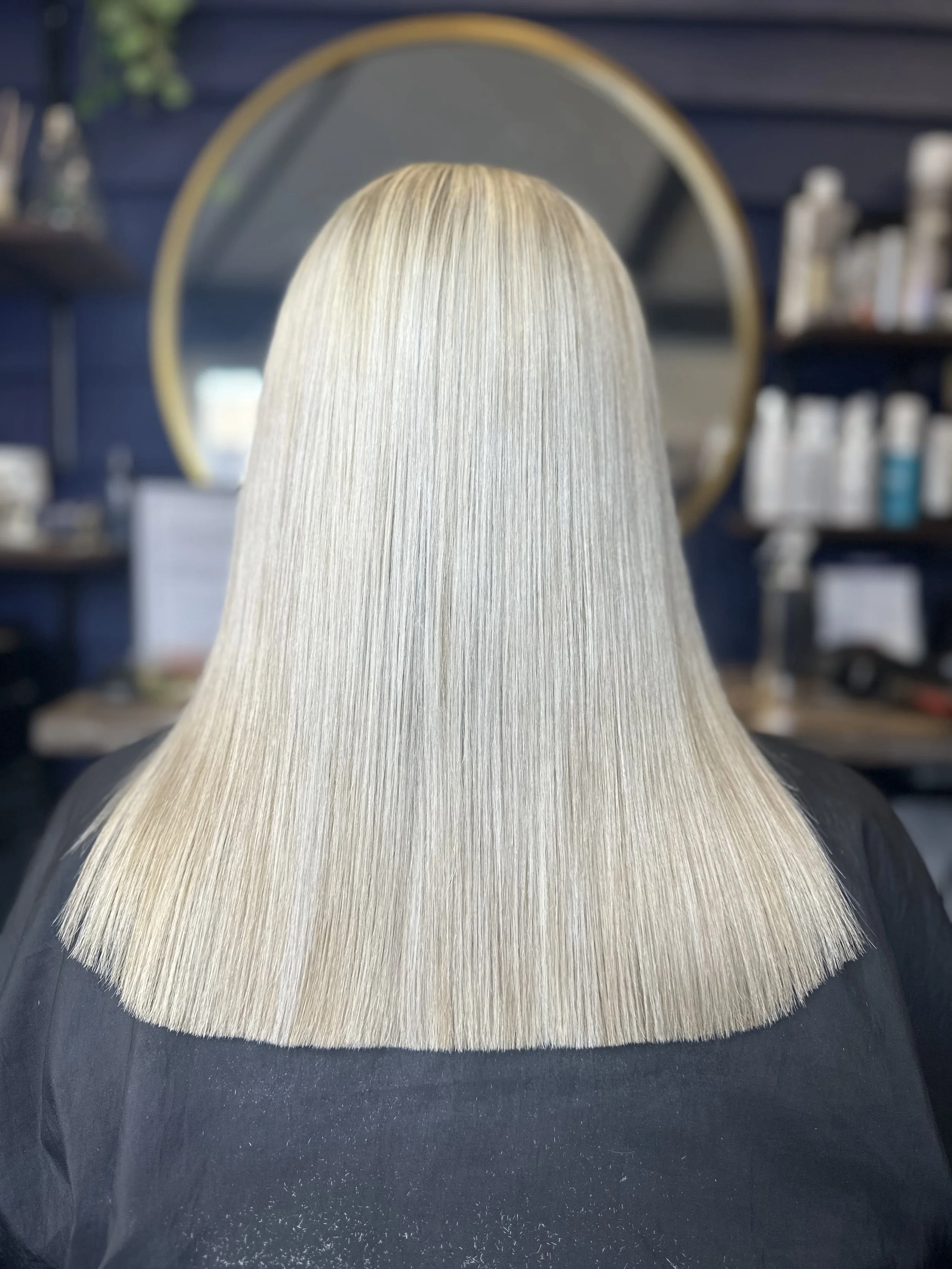 Blonde hair wig on black surface with shelves of hair products in the background