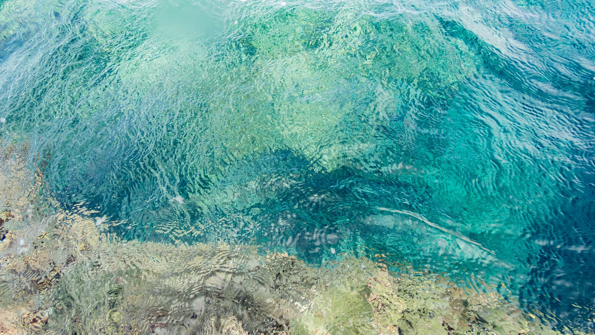 Close-up of ocean water with clear, turquoise waves and ripples over a rocky ocean floor.
