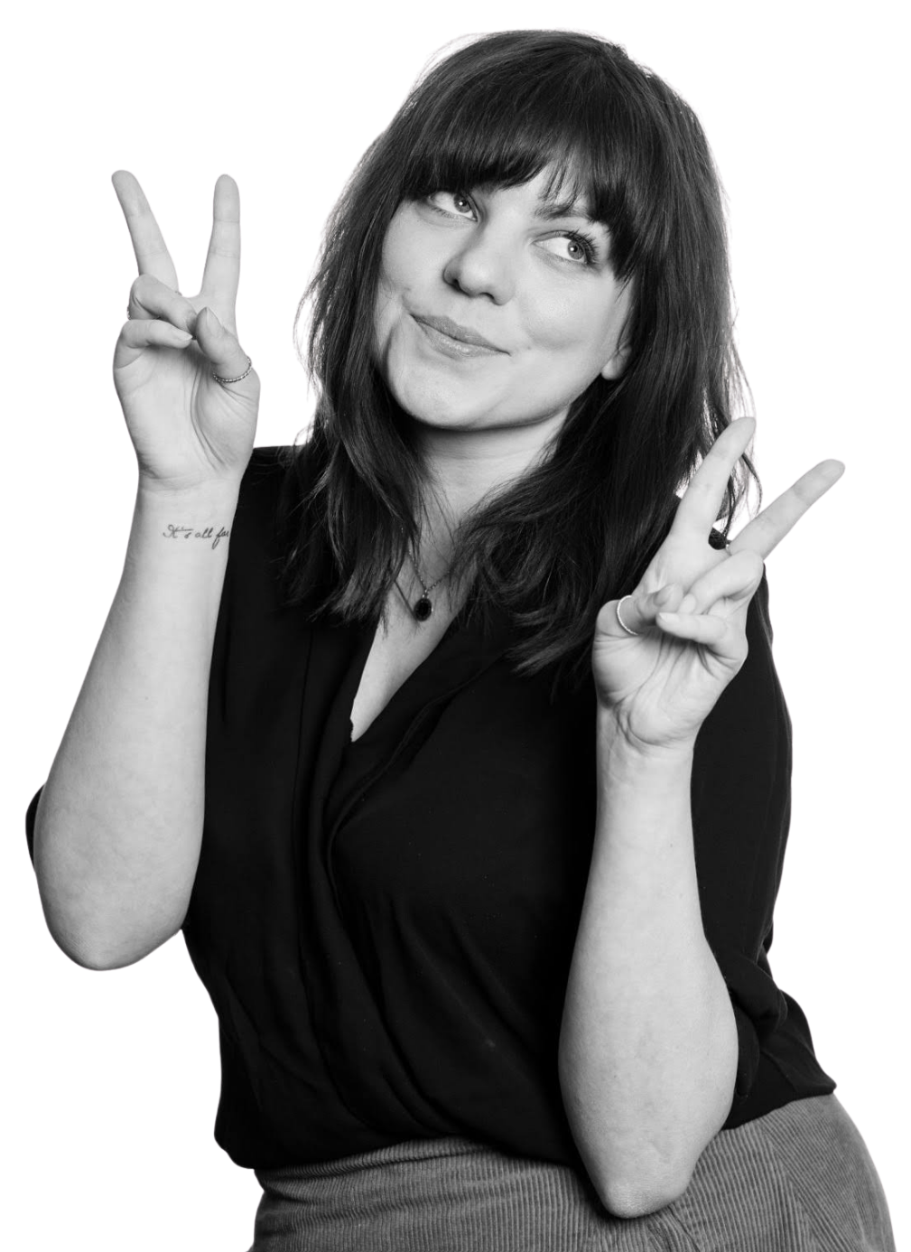 A young woman with shoulder-length dark hair and bangs making a peace sign with both hands and smiling.