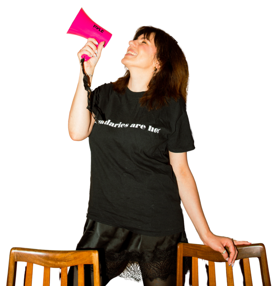 Woman smiling and holding a pink megaphone, standing between two wooden chairs.