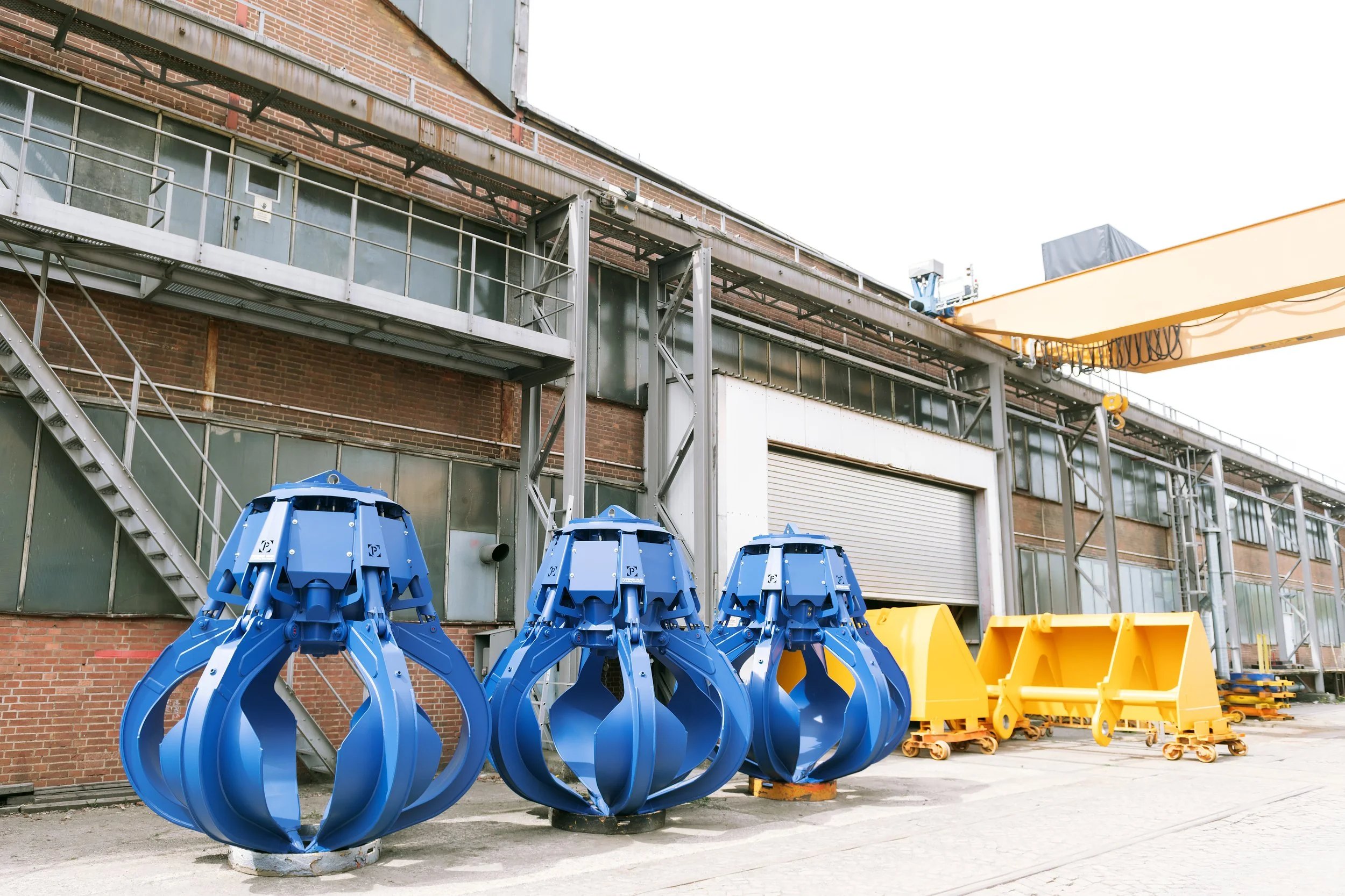 Blaue Baukräne und Baumaschinen vor einem Fabrikgebäude.