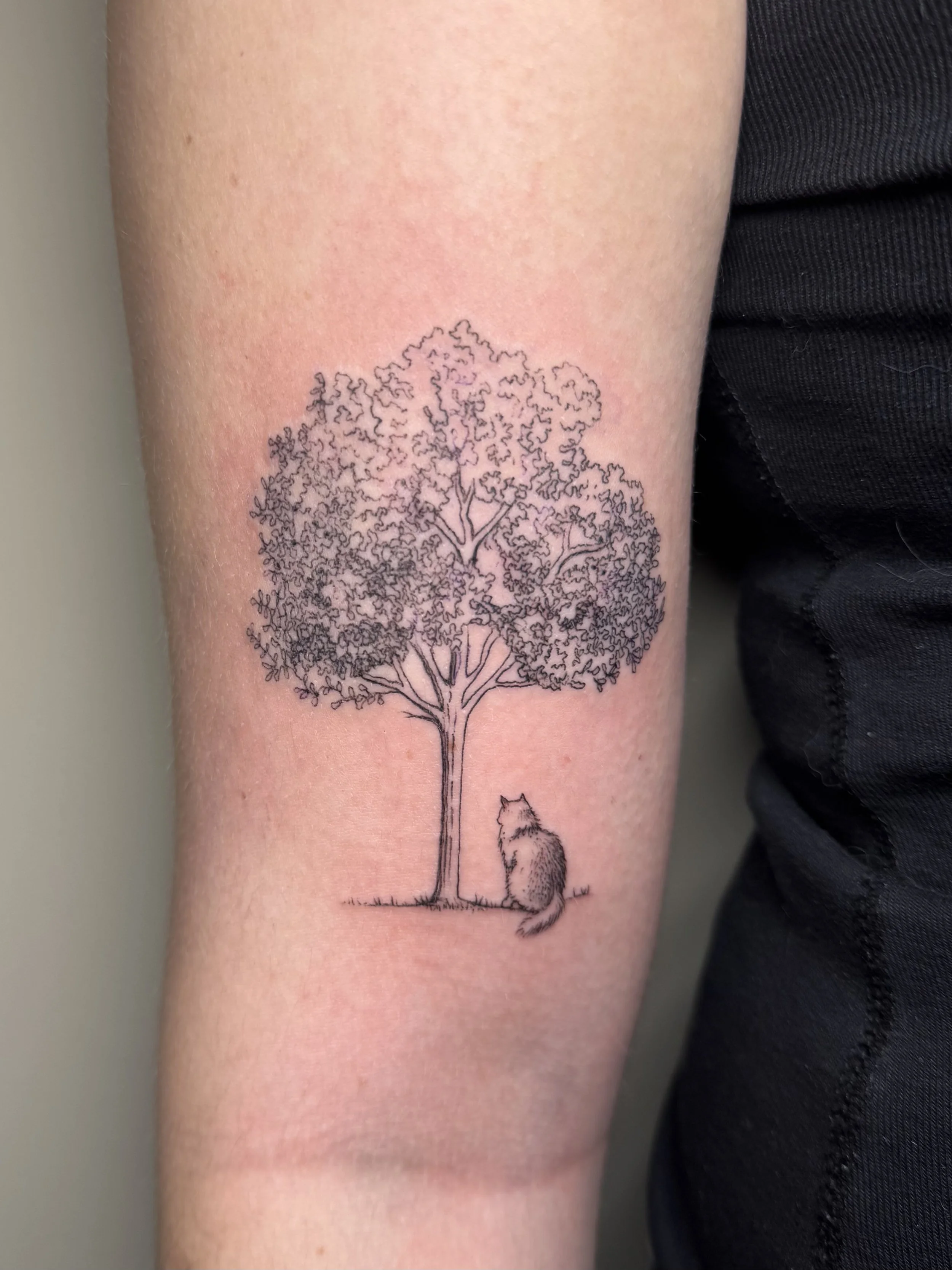 Een tattoo van een boom en een hond op een menselijk voorarm.