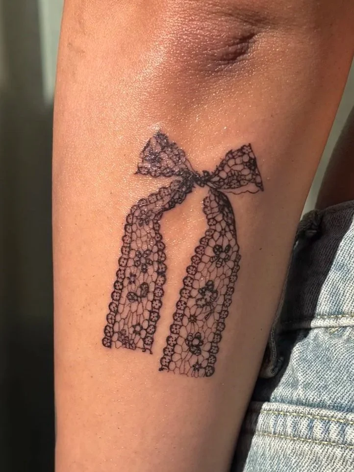 Tattoo van een lace strik op de huid van een arm