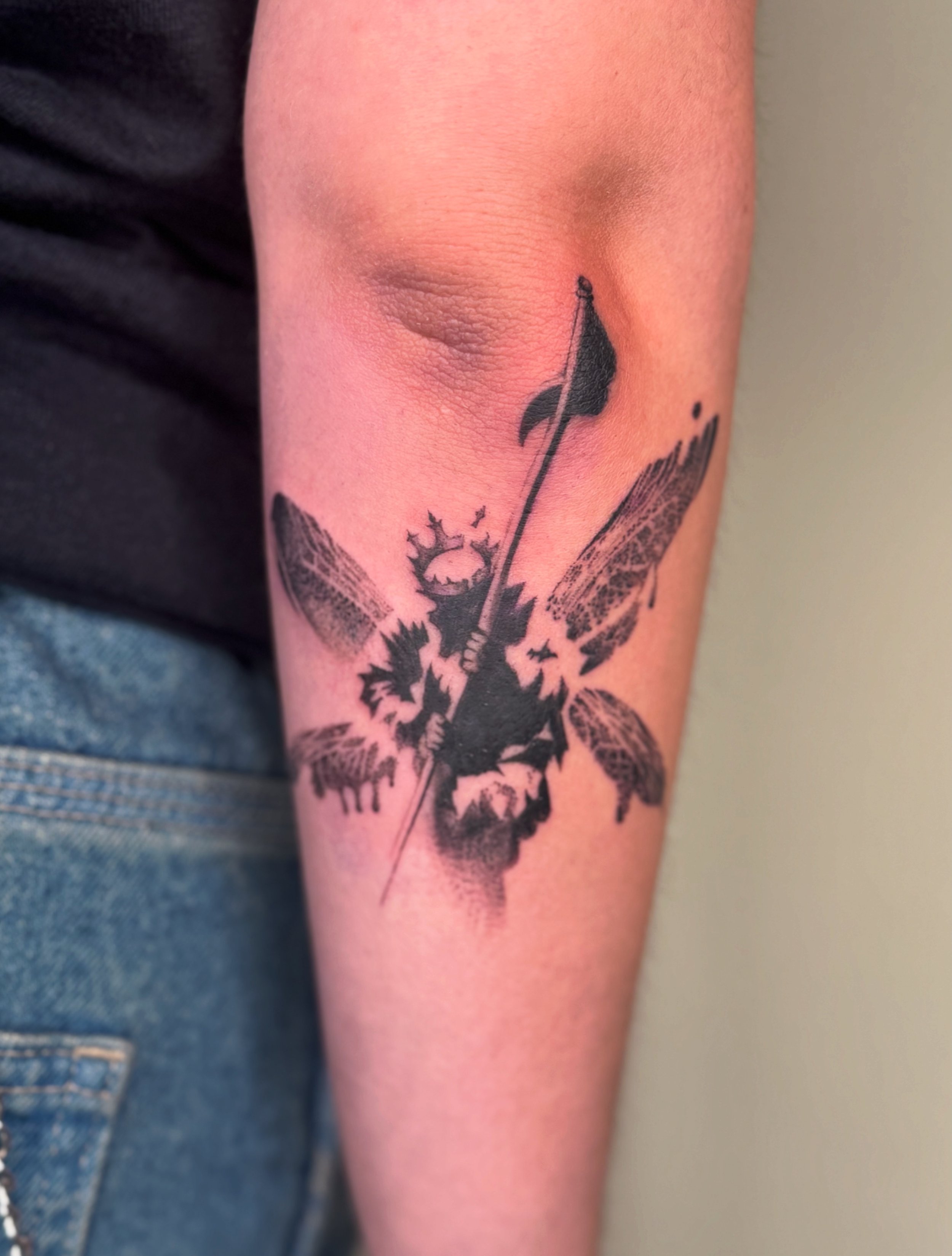Persoon heeft een grote zwarte tatoeage van een vlinder en een zon op de onderarm.