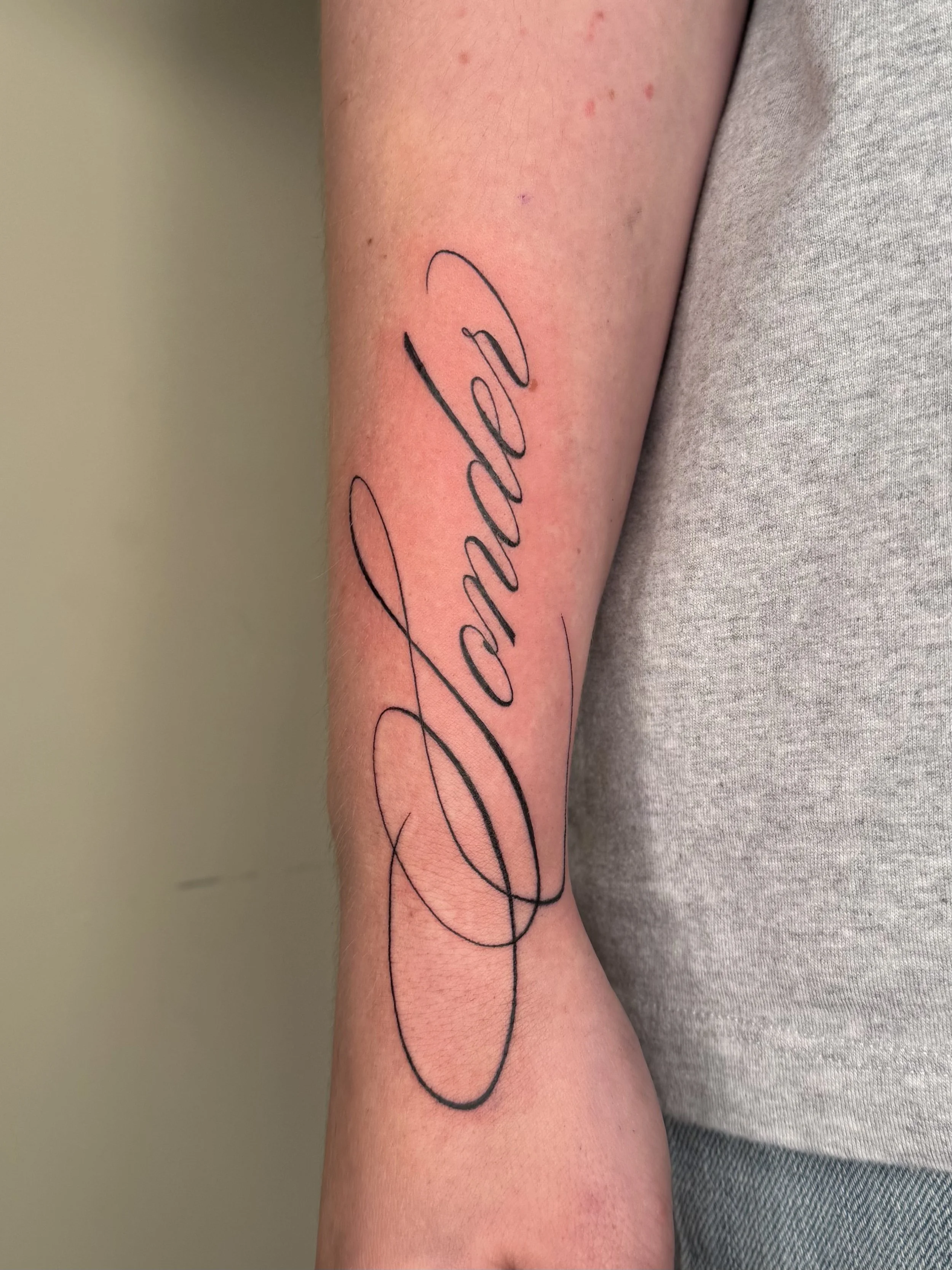 Tattoo van het woord 'Love' in gekalligrafeerde letters op de binnenzijde van de onderarm.
