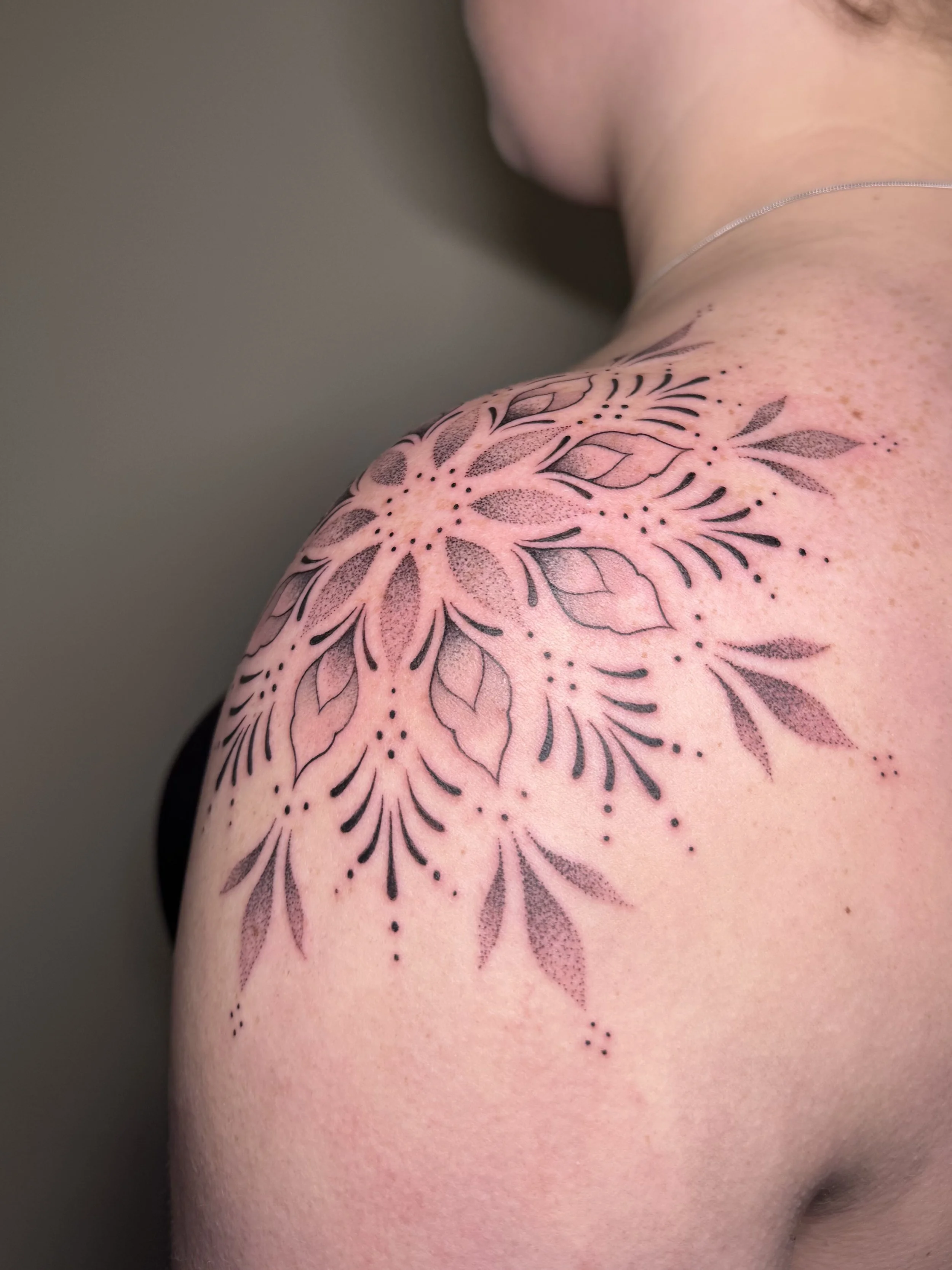 Close-up van een vrouw met een grote, zwarte tattoo van een bloemenpatroon op haar schouder en bovenarm.