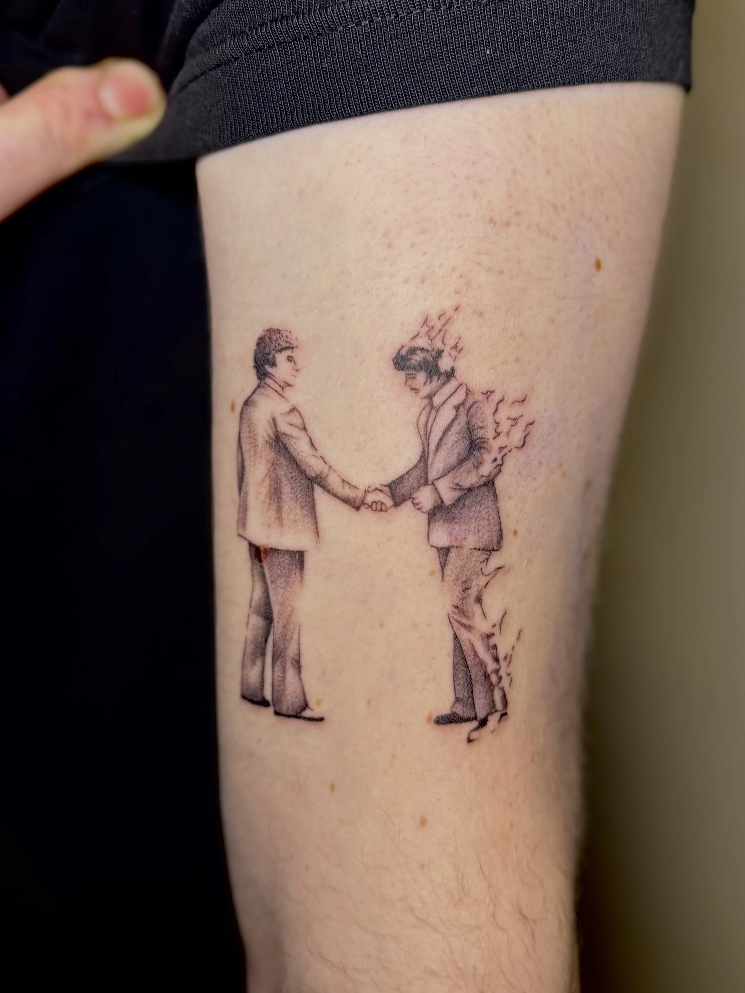 Tatoeage van twee mensen die elkaar de hand schudden, ondertekend met een illegale handdruk.