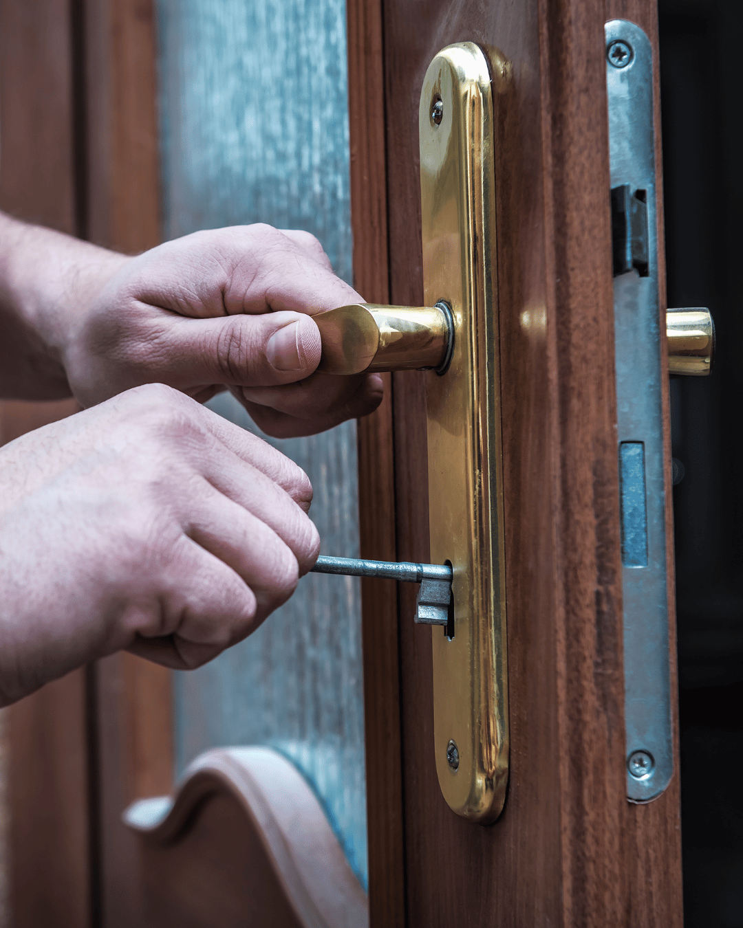 Person inserting a key into a brass door lock on a wooden door.