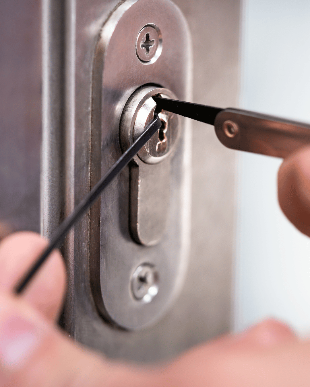 Close-up of a person using a lock picking set to manipulate a lock cylinder on a door lock.