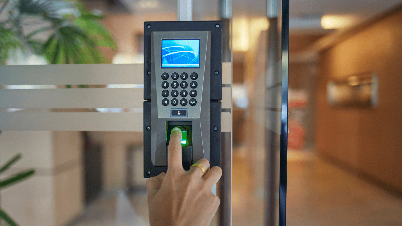 Close-up of a person's hand using a fingerprint scanner to unlock an access control device on a door in an indoor setting.