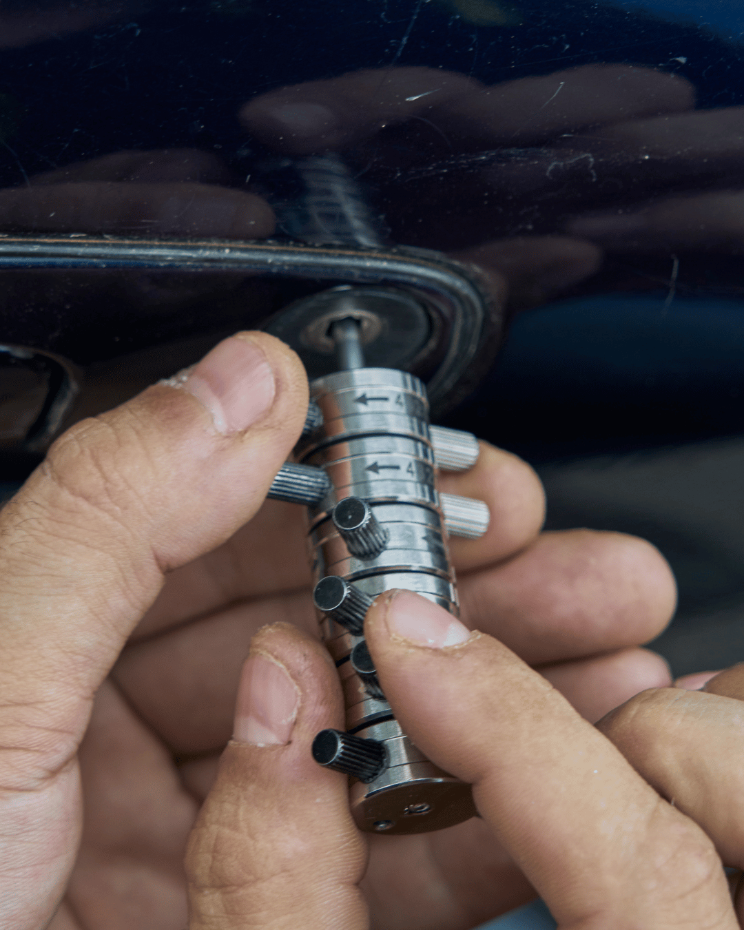 Close-up of a person's hands adjusting a metal timing chain tensioner with a screw tool on a vehicle engine.