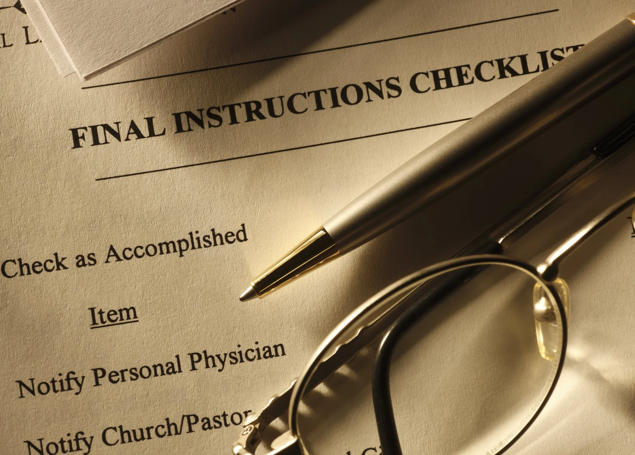 Close-up of a set of files includes final instructions checklist with a silver pen and glasses placed on top of it.