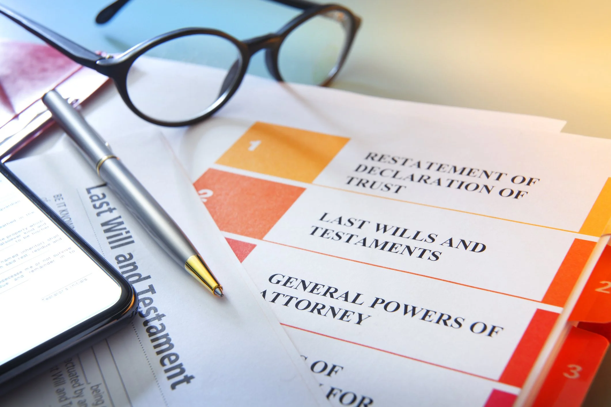 Close-up of a legal document along with a silver pen placed on top, a pair of glasses, and a cellphone nearby on a desk, with papers underneath.