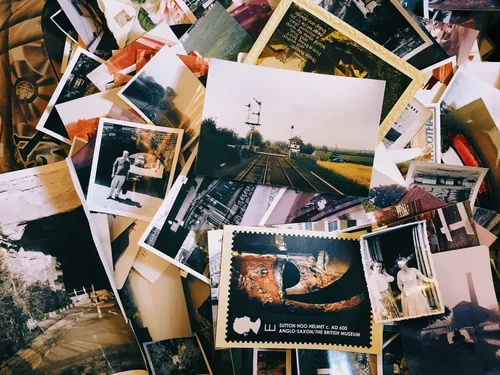 A pile of scattered photographs and postcards, including a train track scene, a person standing outside, and a stamp from Sutton Hood Museum.